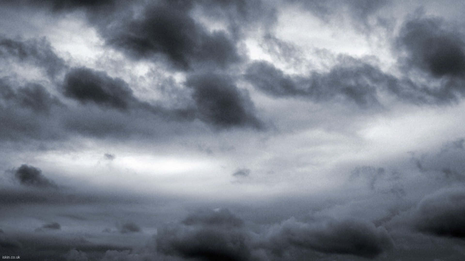高解析度陰鬱天空 壁紙 — 戲劇性的暴風雲在陰沉的灰色天空中翻騰，有明亮的陽光斑塊穿透雲層。