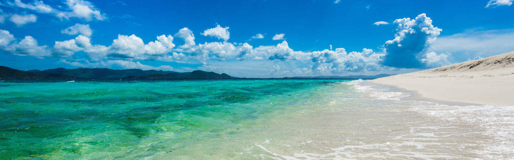 高解析度雙螢幕海灘沙灘背景 壁紙 — 清澈碧綠的海水輕拍著純淨的白色沙灘，上方是湛藍的天空和蓬鬆的白雲。