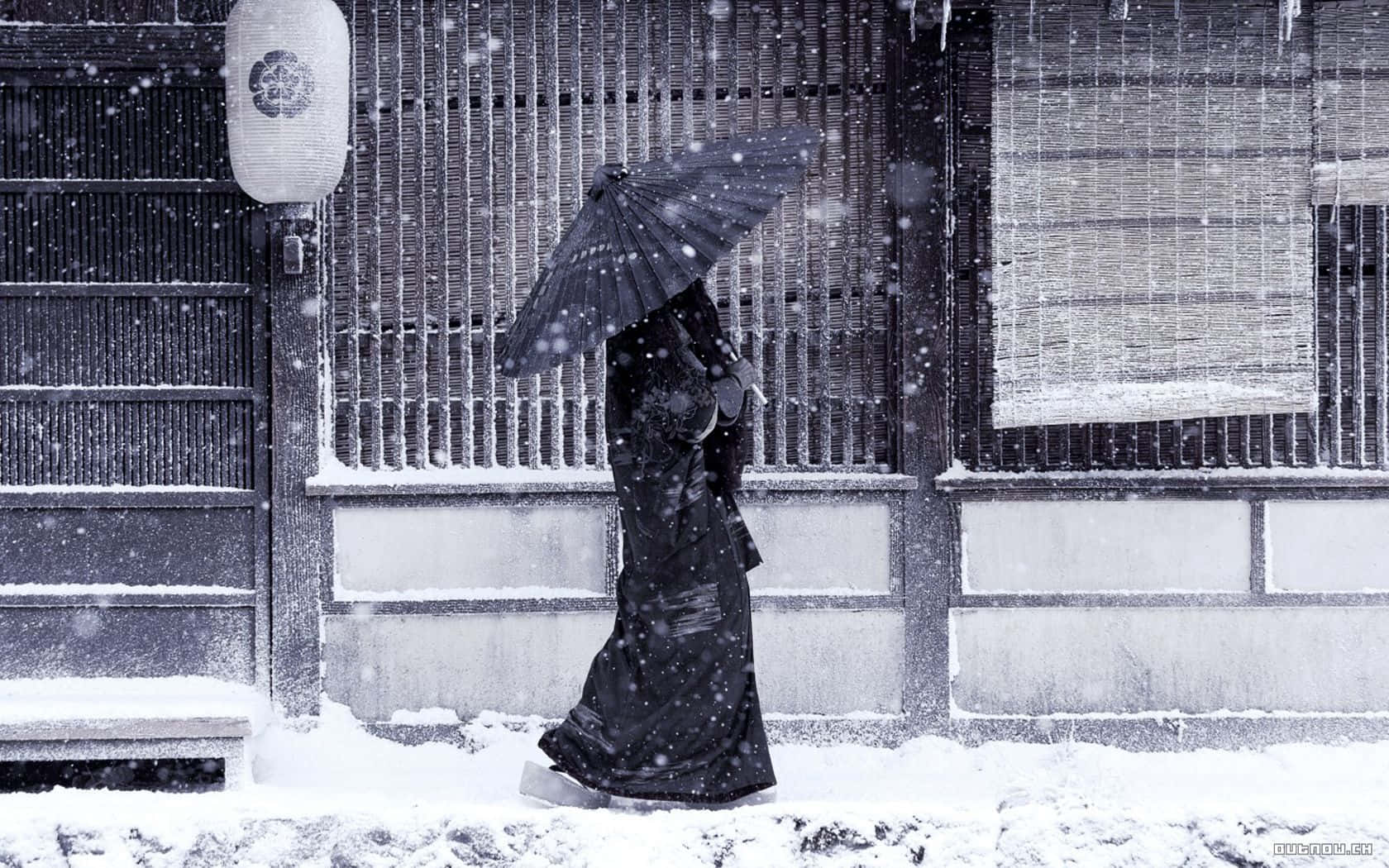 穿黑色和服撐傘的人走在雪中，靠近傳統日式建築。
