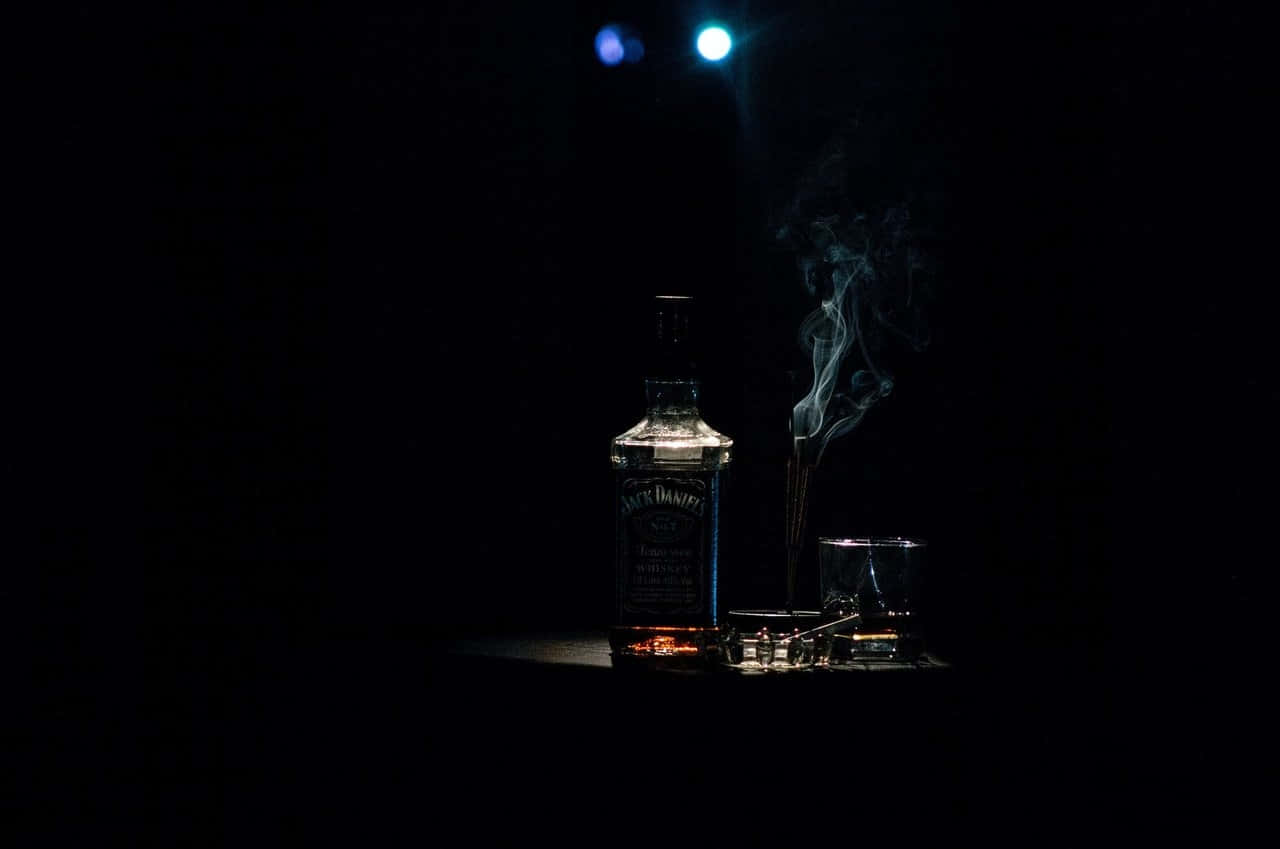 Jack Daniel's威士忌瓶和玻璃杯被聚光燈照亮，煙霧在黑暗中升起。
