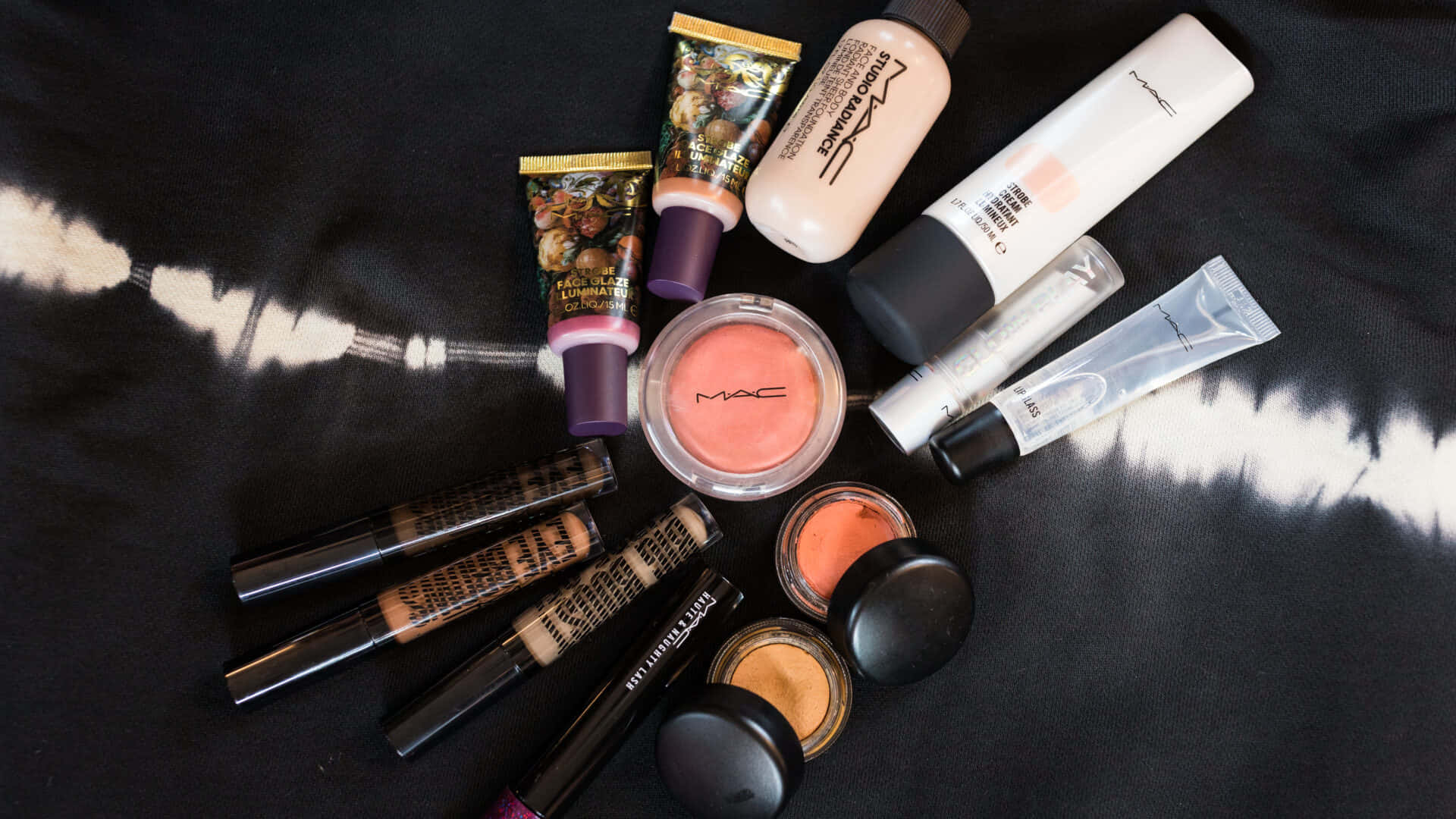 高質感專業彩妝 — Mac Cosmetics 壁紙 — 在黑白紮染布料背景上排列的MAC化妝品平鋪圖。