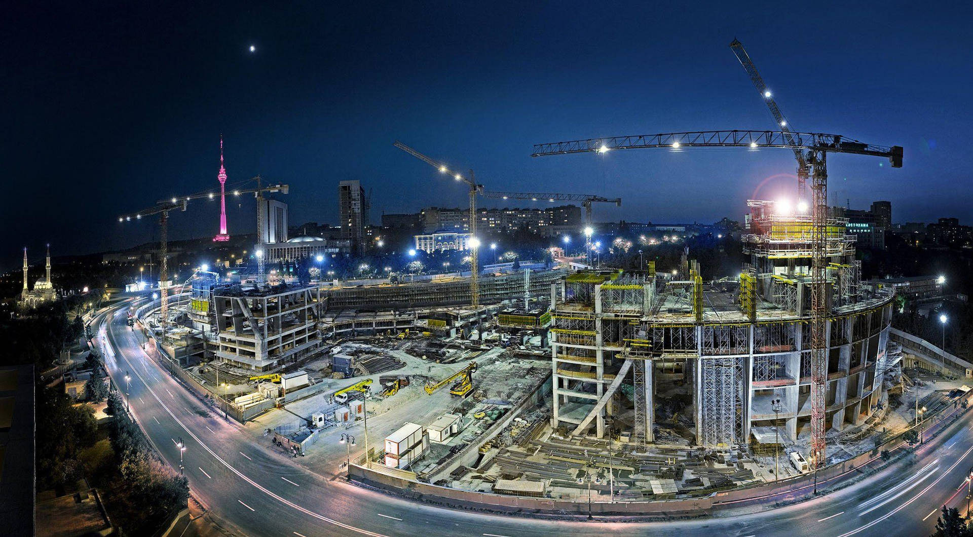 夜間城市建築工地，有起重機和發光塔樓。