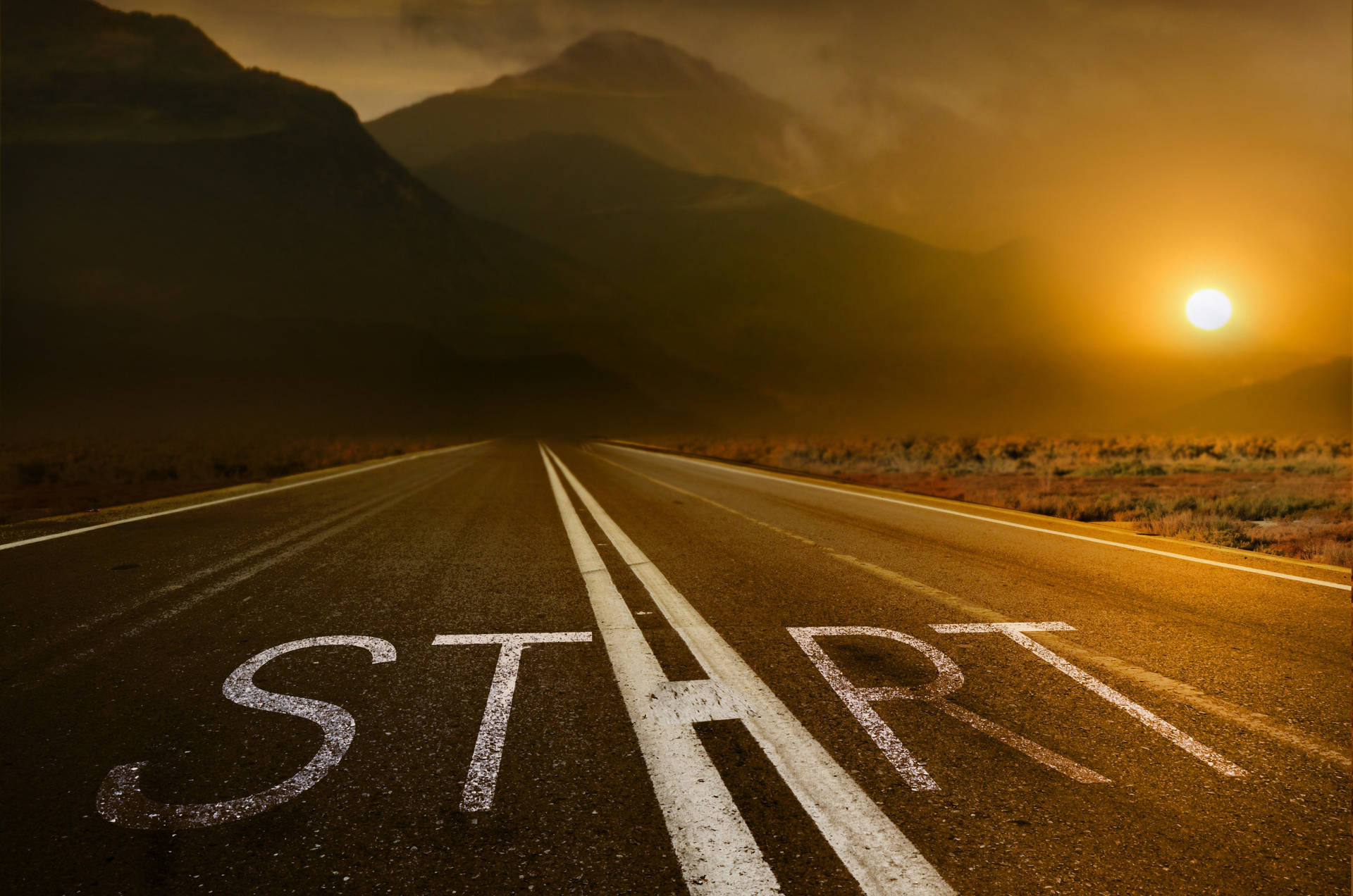 一條穿過山脈的道路，日落時分瀝青上塗有「START」。