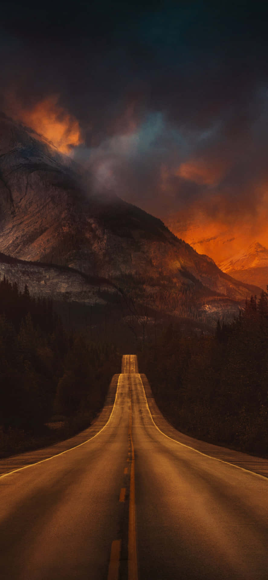 一條蜿蜒穿過森林的道路在戲劇性的暮色天空下通往群山。