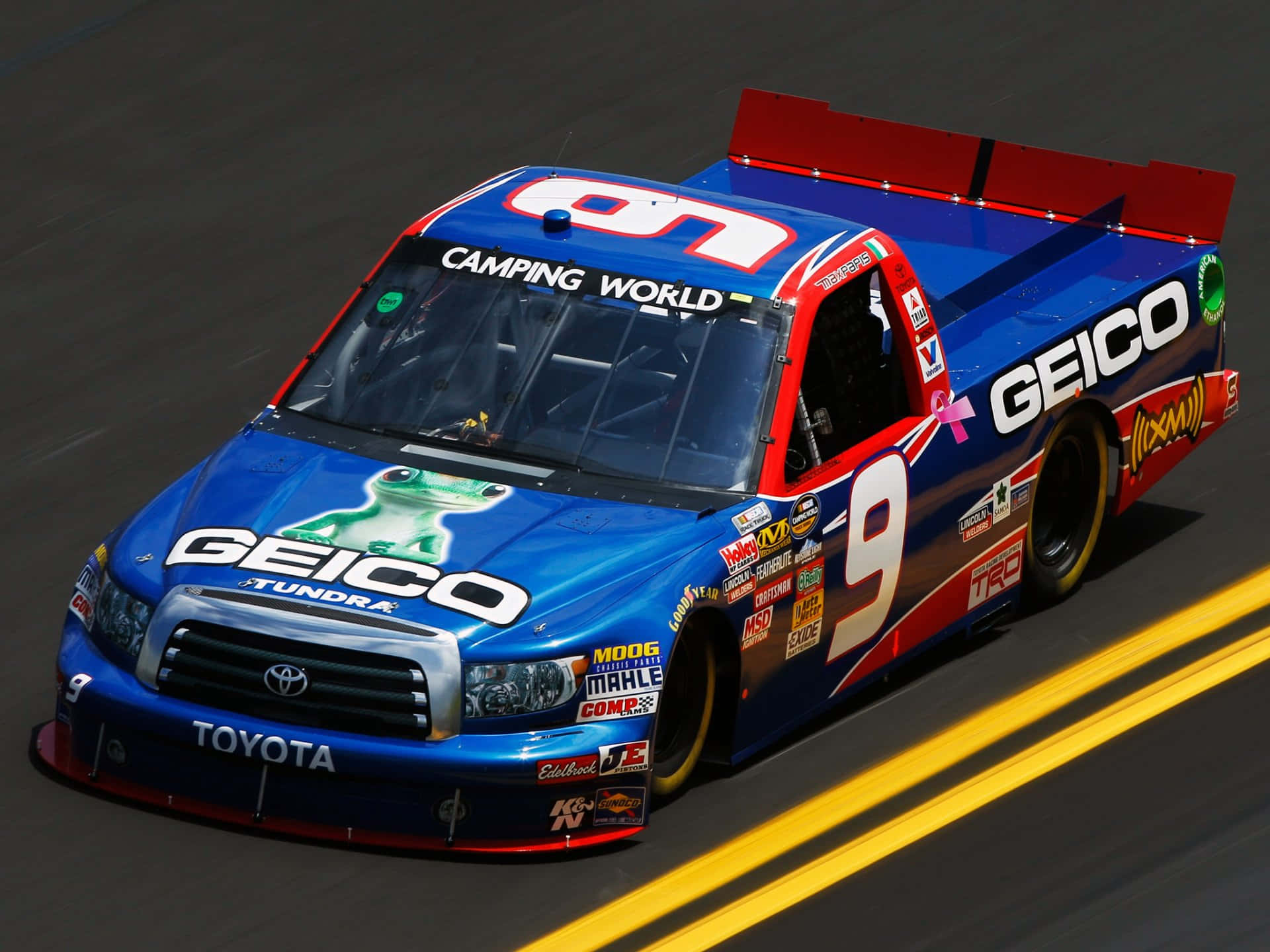 帶有 GEICO 標誌的藍色和紅色 NASCAR 賽車卡車在賽道上飛馳。