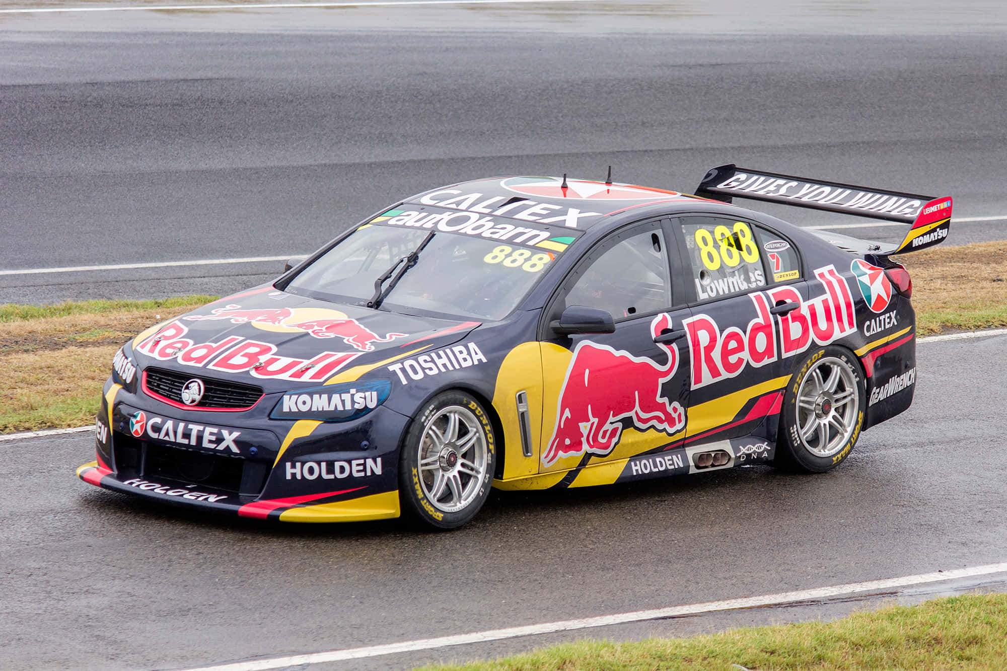 高速刺激：賽車在賽道上競速 壁紙 — 一輛編號888的Red Bull Racing Holden V8 Supercar在多雲的天空下沿著濕滑的賽道疾馳。