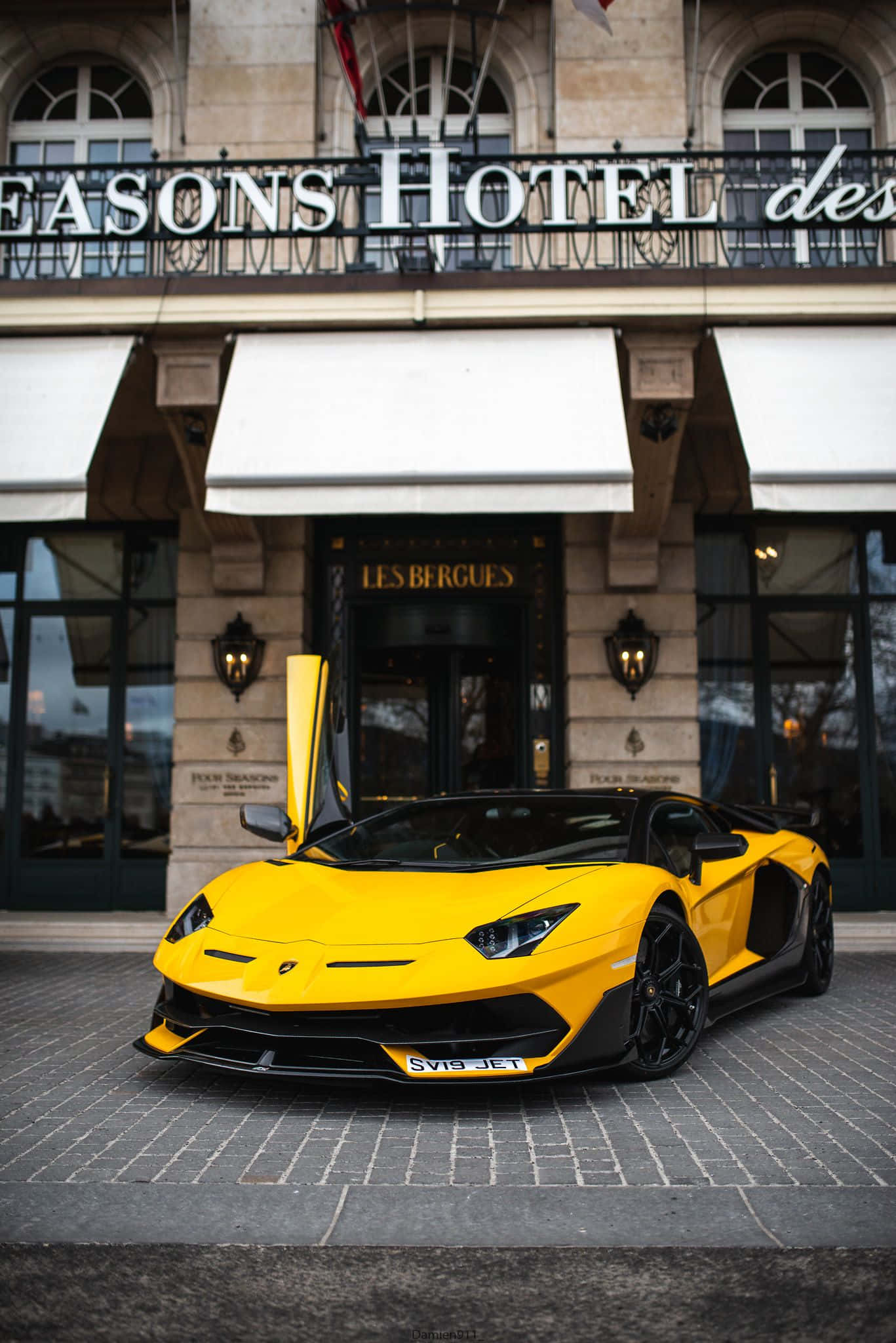 高速刺激賽車體驗 壁紙 — 一架鮮黃色林寶堅尼 Aventador 配備鷗翼車門，停泊在豪華酒店門前的鵝卵石路上。