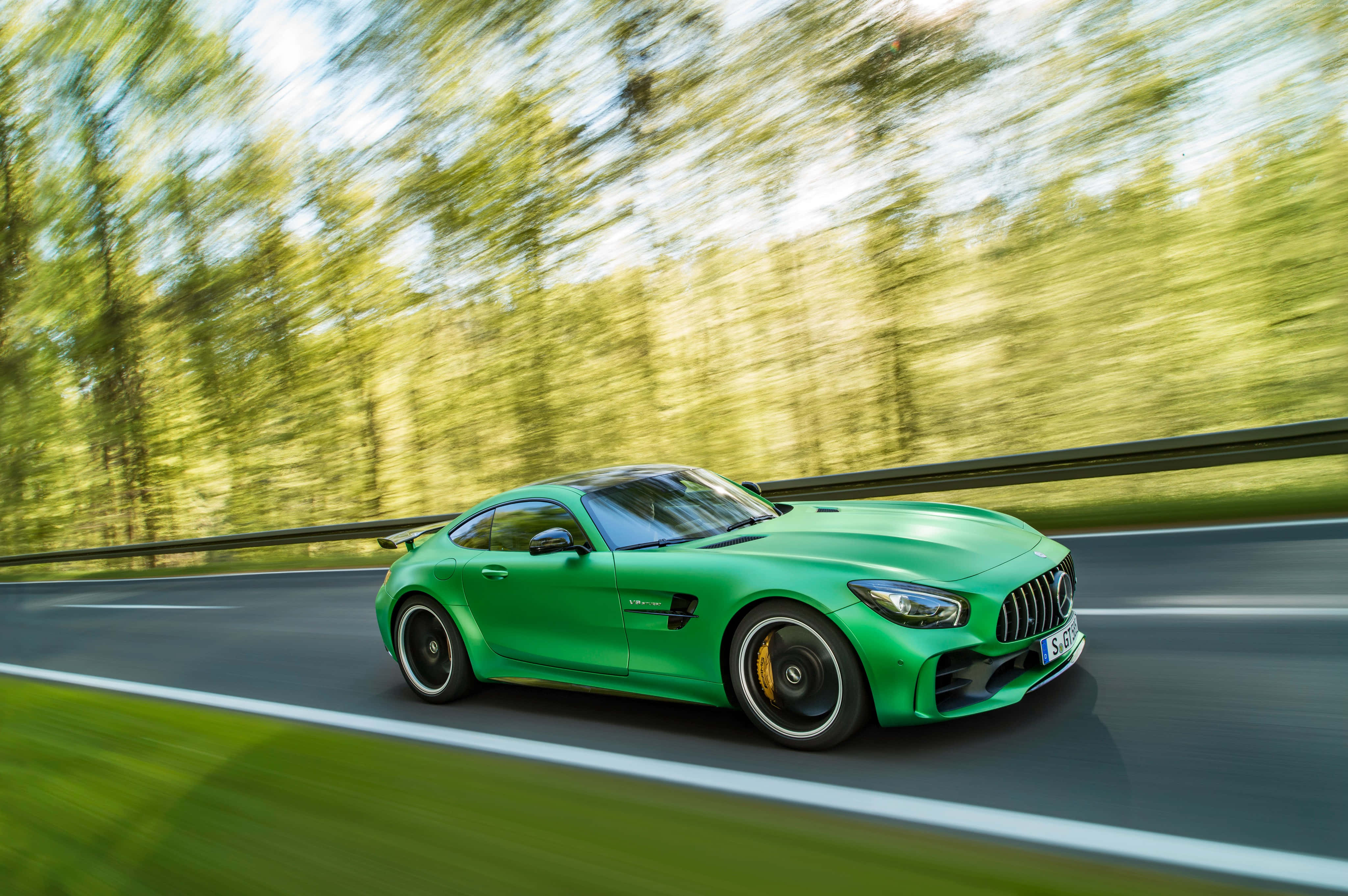 高速行駛的綠色梅賽德斯-AMG GT R搭配綠樹背景 壁紙 — 一輛充滿活力的綠色跑車在森林環繞的道路上疾馳，動態模糊強調了它的速度。