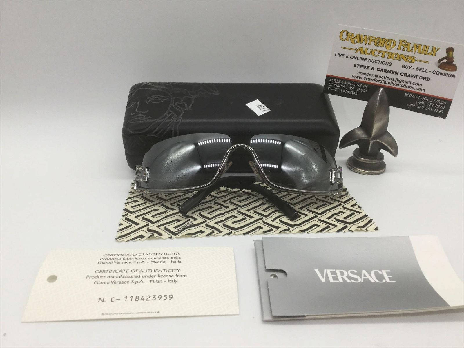 高雅 Versace 環繞式太陽眼鏡 壁紙 — 一套時尚的黑色 Versace 太陽眼鏡，連同原裝眼鏡盒、證書及品牌包裝，展示在圖案布上。