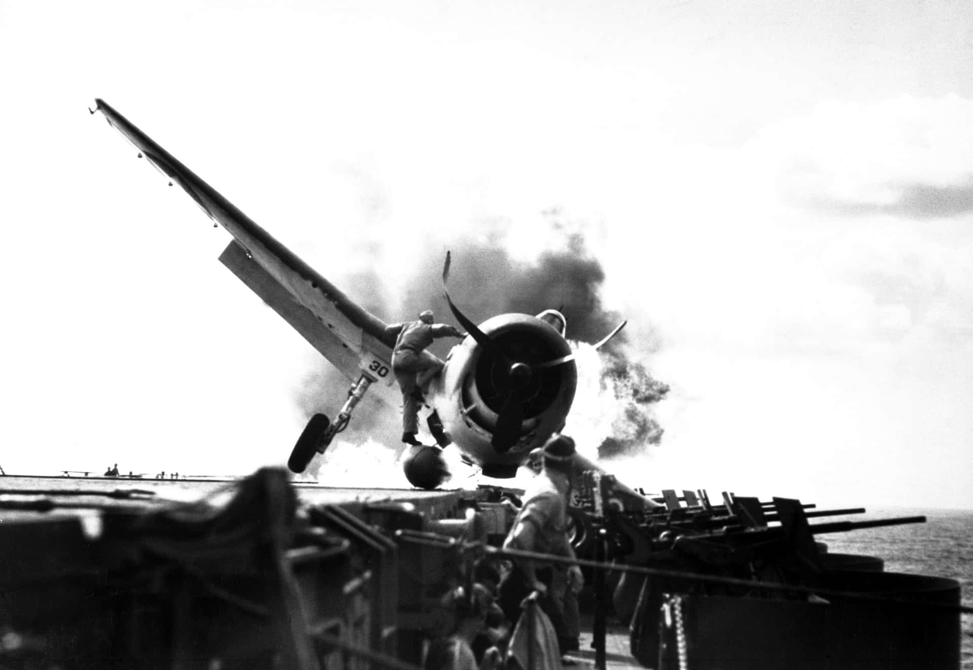 航空母艦甲板上燃燒的飛機，附近有船員。
