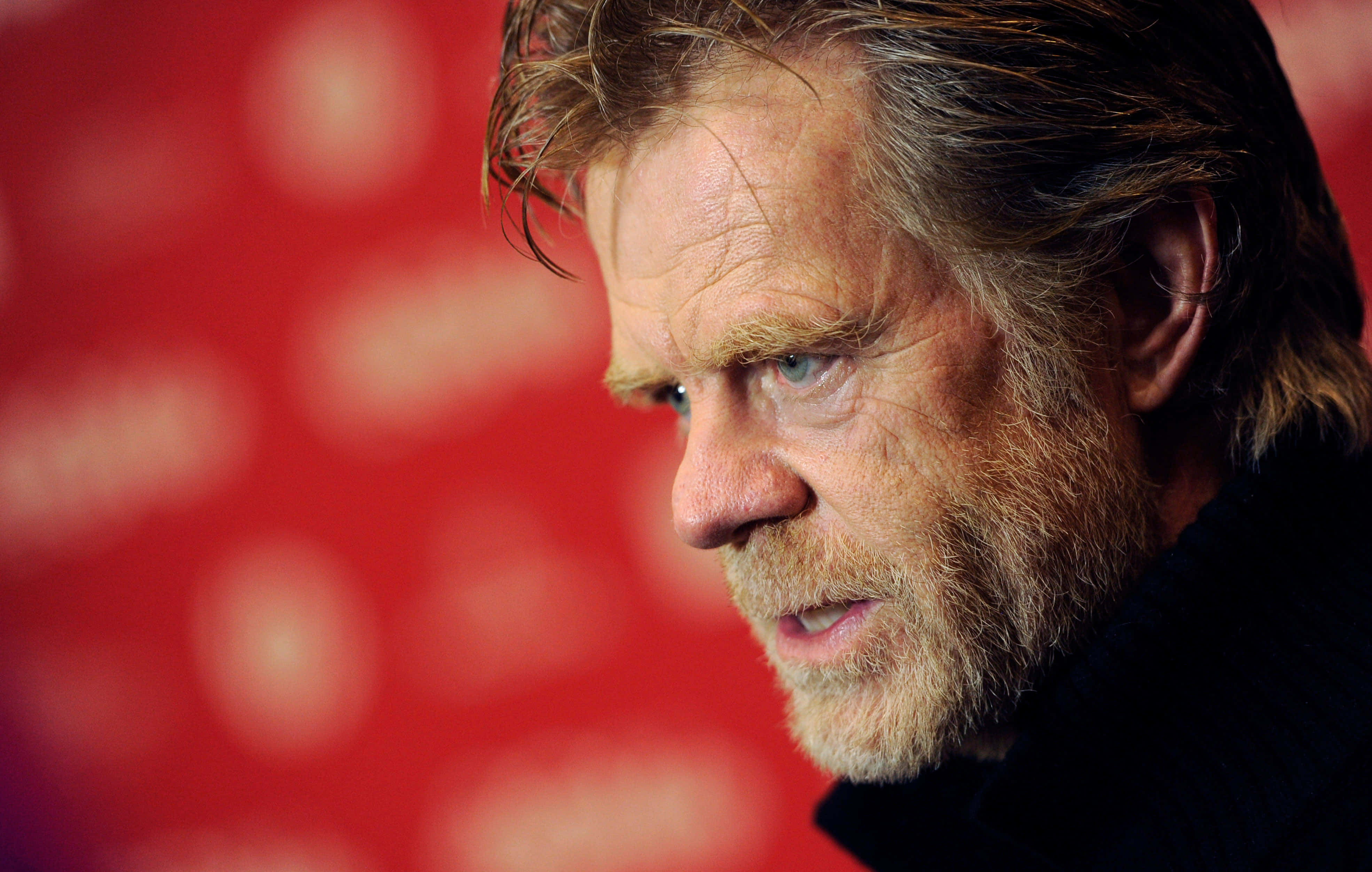 william h. macy 桌布 壁紙 — 鬍鬚男嘅近距離肖像，眼神強烈，背景係模糊嘅紅色。