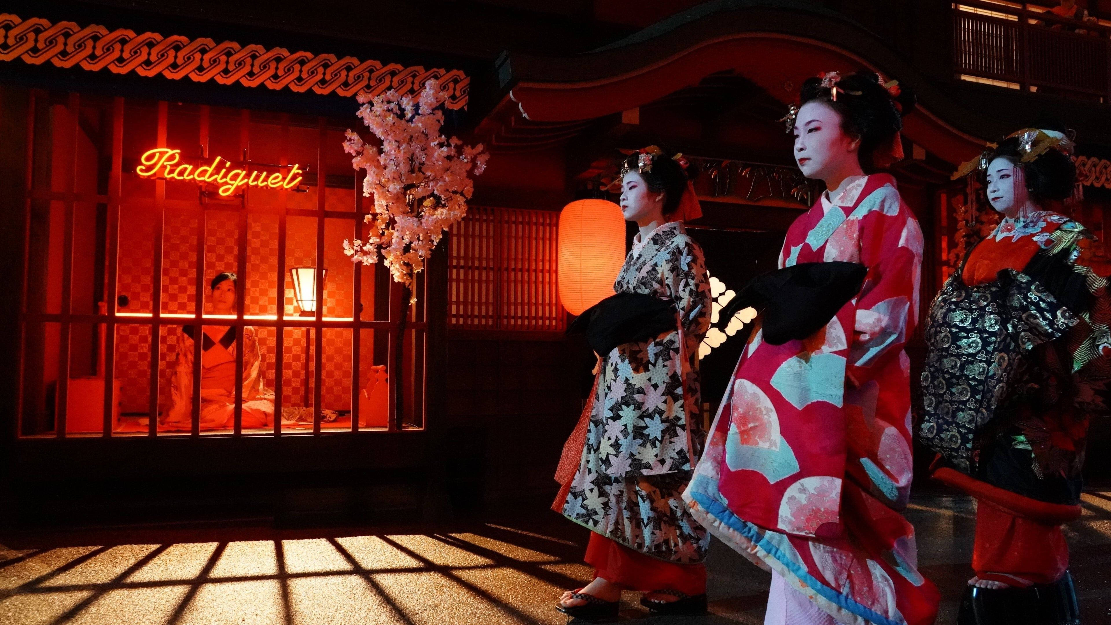 《鬼域囚徒》日本女性 壁紙 — 三位穿著鮮豔和服的藝妓，在黃昏時分站在一座霓虹燈閃爍的傳統日本建築前。