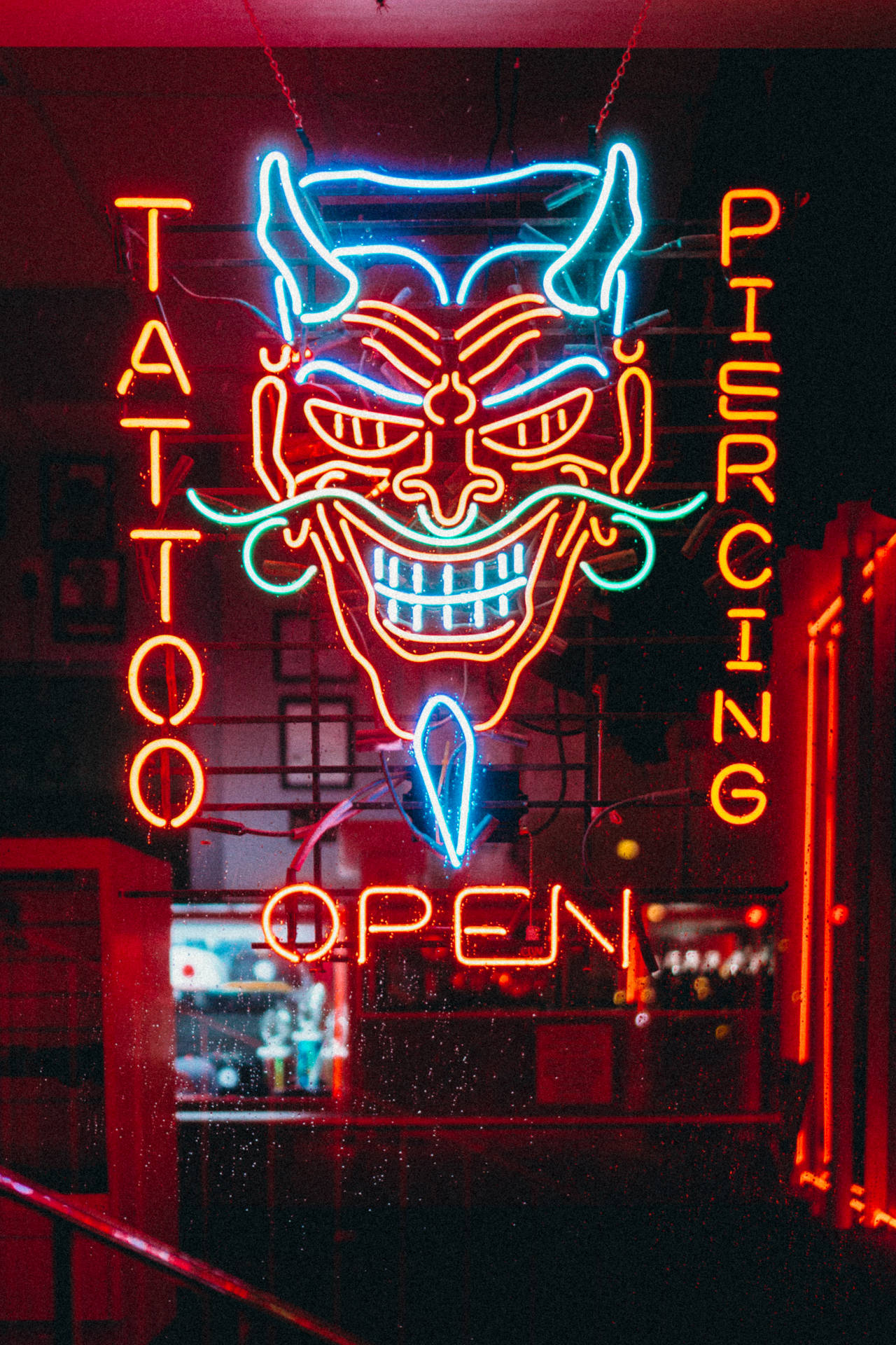 紋身和穿孔店的霓虹燈牌，惡魔面孔在夜晚發出紅藍光芒。