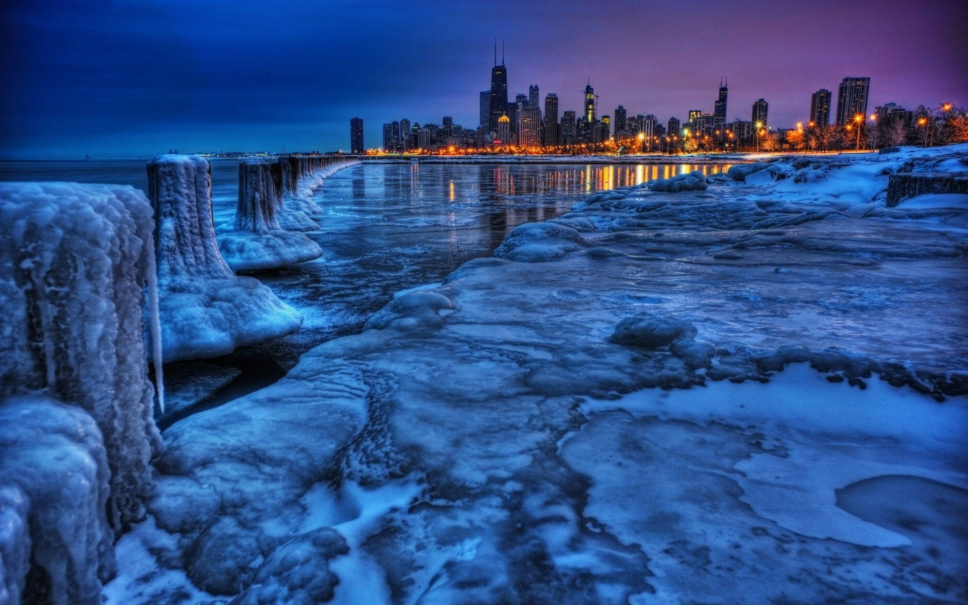 冰封的河岸，冰層結構與城市燈光在暮色中倒映於水面。