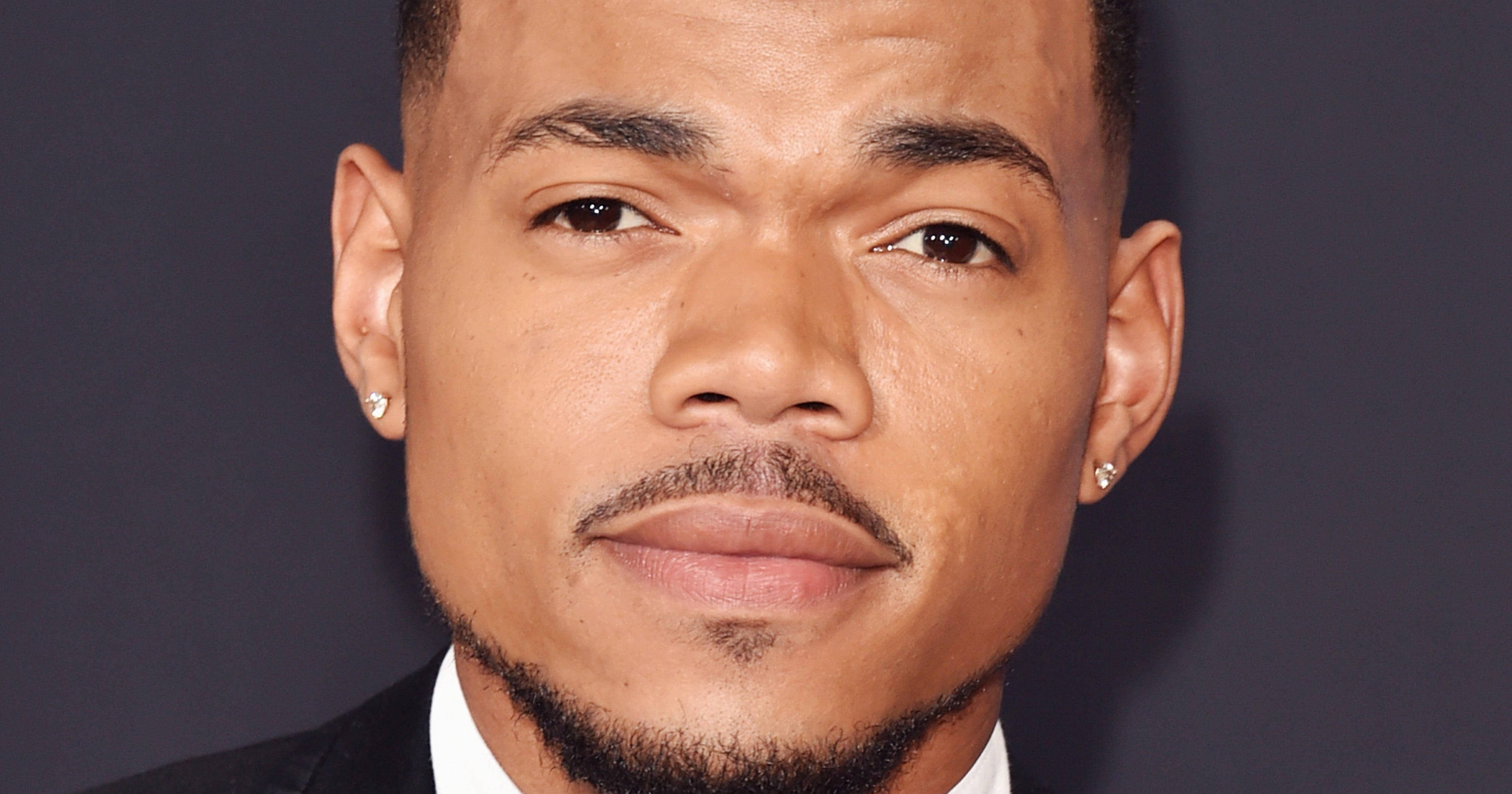 魅力四射的 Chance The Rapper 壁紙 — 一名表情嚴肅的男子戴著鑽石耳釘和西裝，以深灰色背景為襯的特寫肖像。