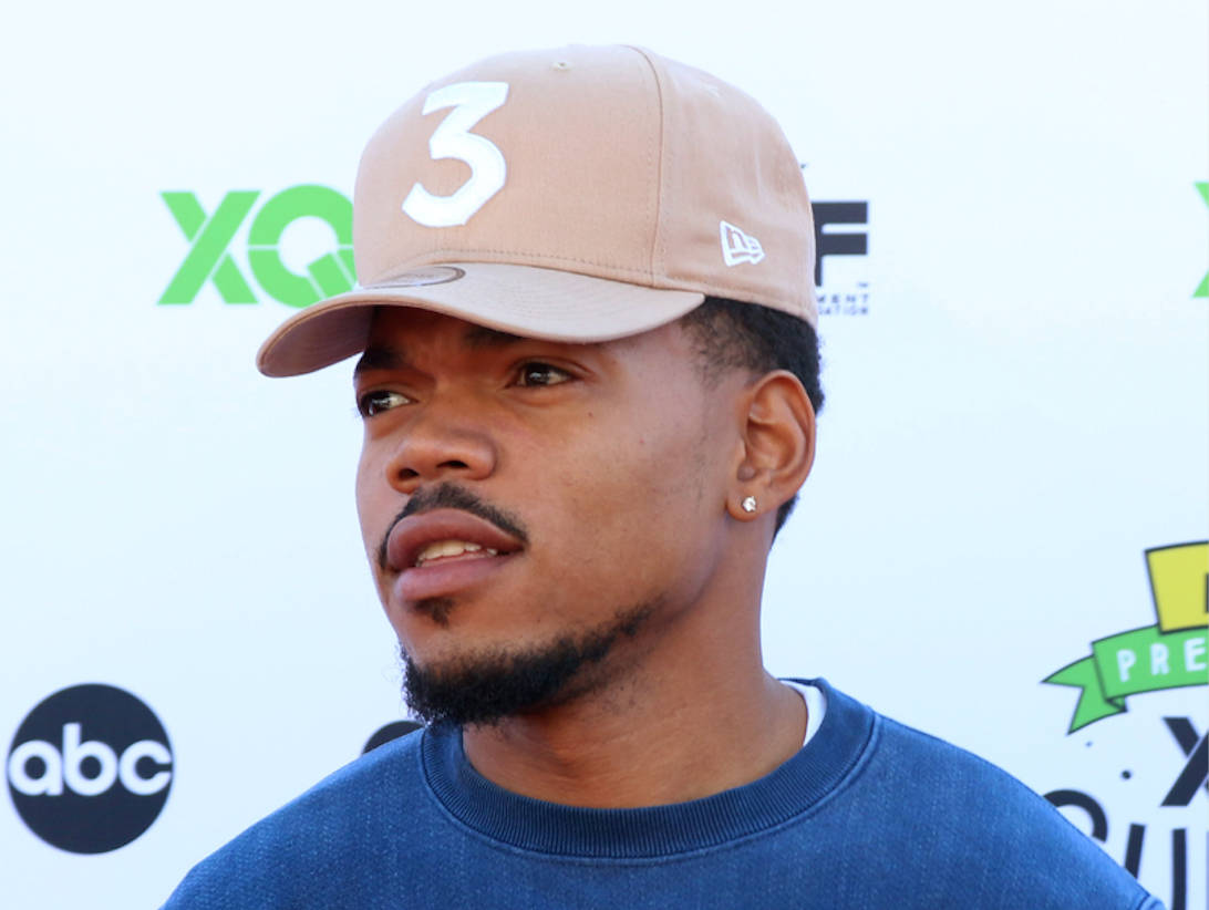 魅力四射的 Chance The Rapper 壁紙 — 一名戴著米色帽子、上面有白色數字三、身穿藍色運動衫的男子站在帶有標誌的背景前。