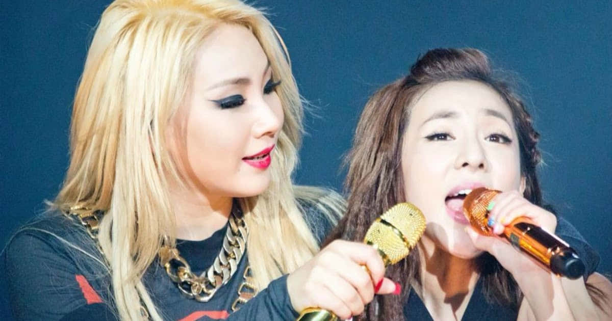 兩位女K-pop歌手在舞台上拿著麥克風表演。