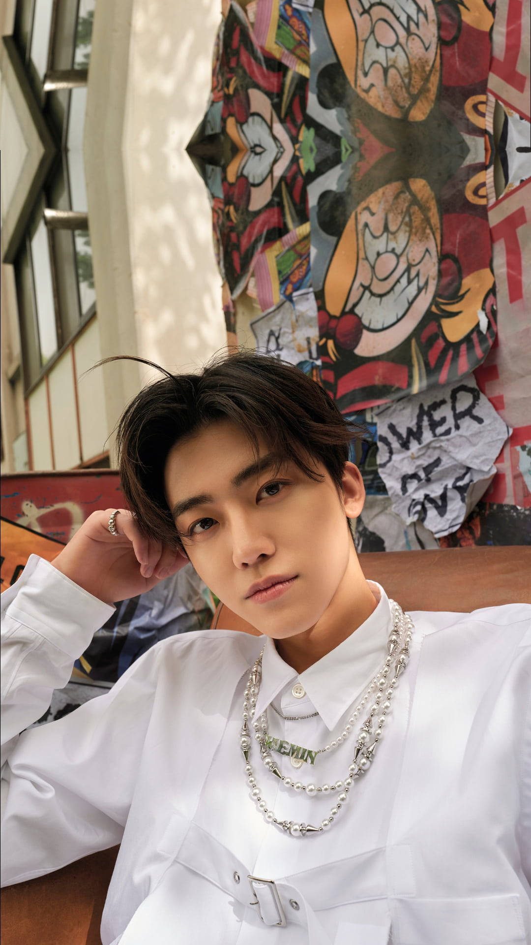 魅力滿點 Jaemin NCT 周圍環繞鮮豔海報牆 壁紙 — 一位身穿白色襯衫和層疊銀鏈的年輕男子，在色彩繽紛的卡通臉塗鴉牆前擺姿勢。