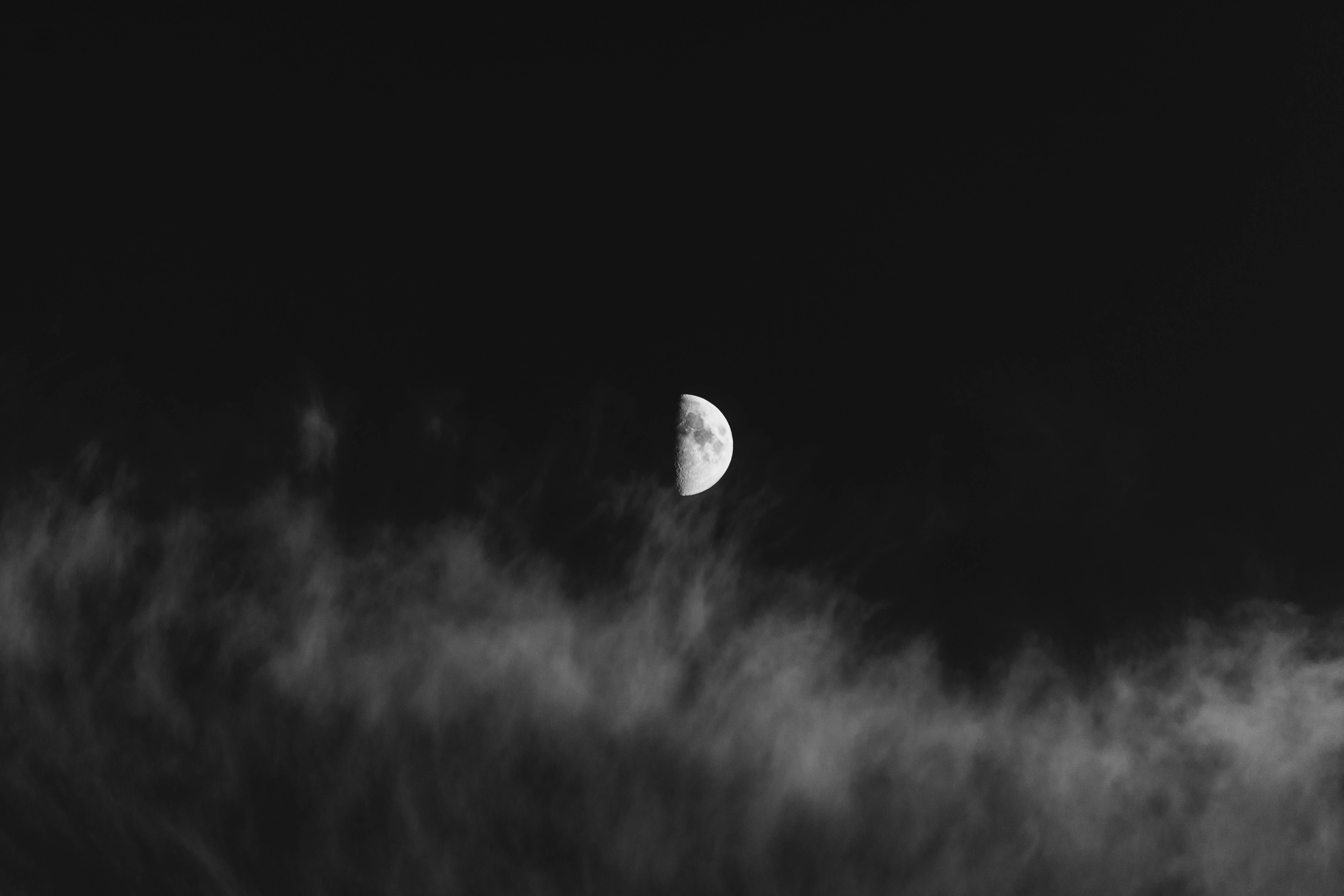 魅惑半月暗調4K 壁紙 — 一彎新月在濃密的霧雲層上柔和地發光，映襯著鮮明的黑白夜空。