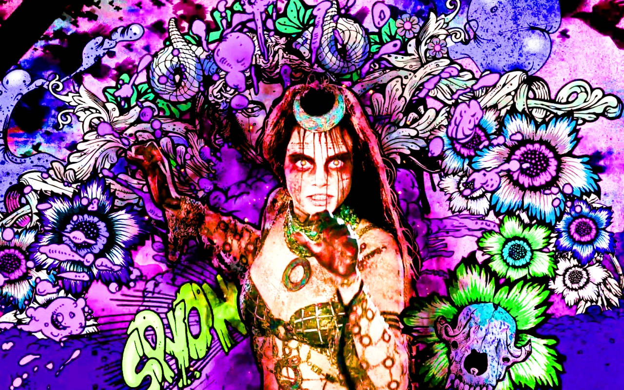 魅惑女巫立於花卉塗鴉牆 壁紙 — 一位風格化的女性，擁有發光的眼睛和華麗的紋身，站在紫色、藍色和綠色花朵與頭骨的迷幻爆炸之中。