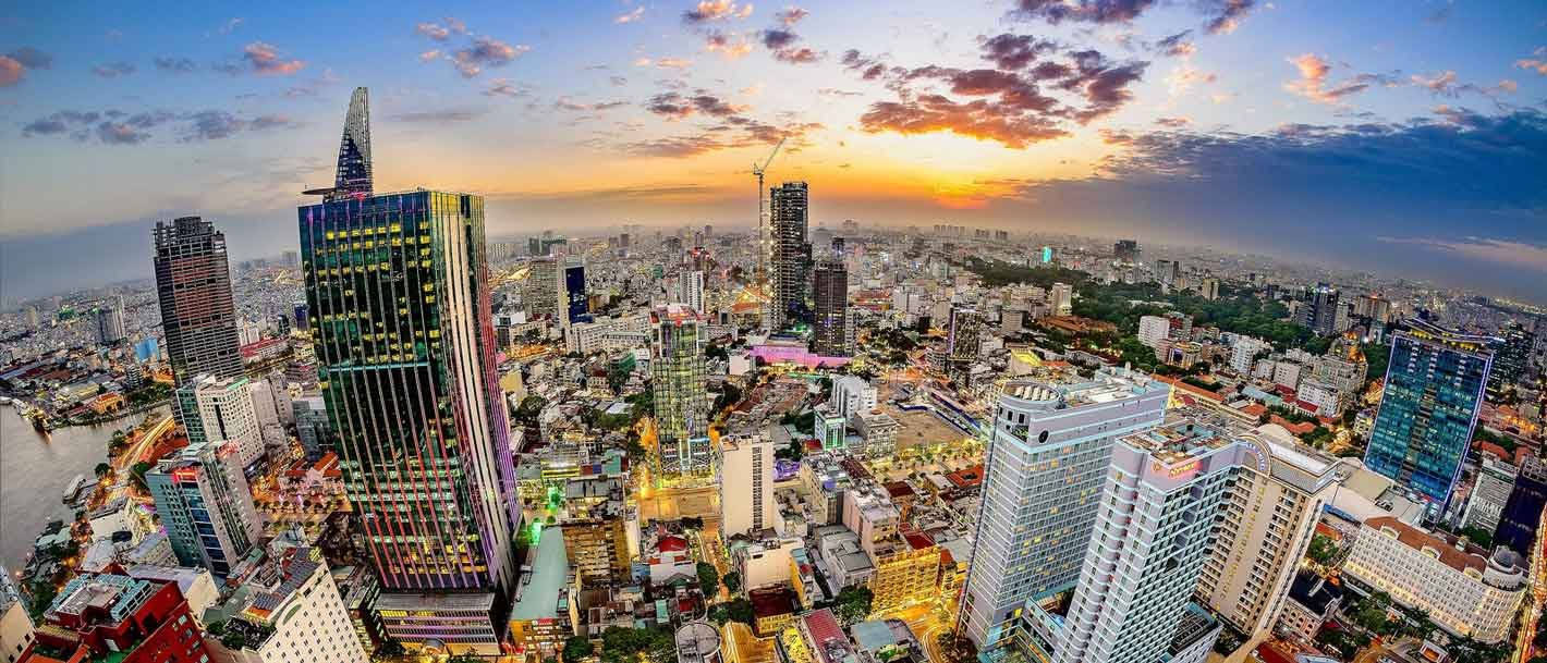 魚眼鏡頭下的胡志明市動感風光 壁紙 — 日落時分繁忙城市景觀的鳥瞰圖，高聳的摩天大樓和閃爍的燈光映襯著充滿活力的橙色和紫色天空。