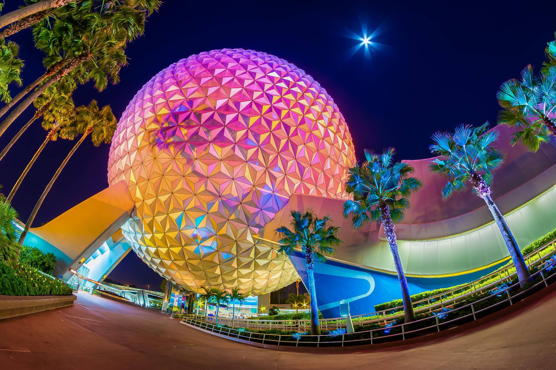 魚眼鏡頭下的色彩繽紛Epcot地球儀與棕櫚樹 壁紙 — 一個充滿活力的測地線球體在棕櫚樹環繞的星空下閃爍著粉紅色和金色的光芒。