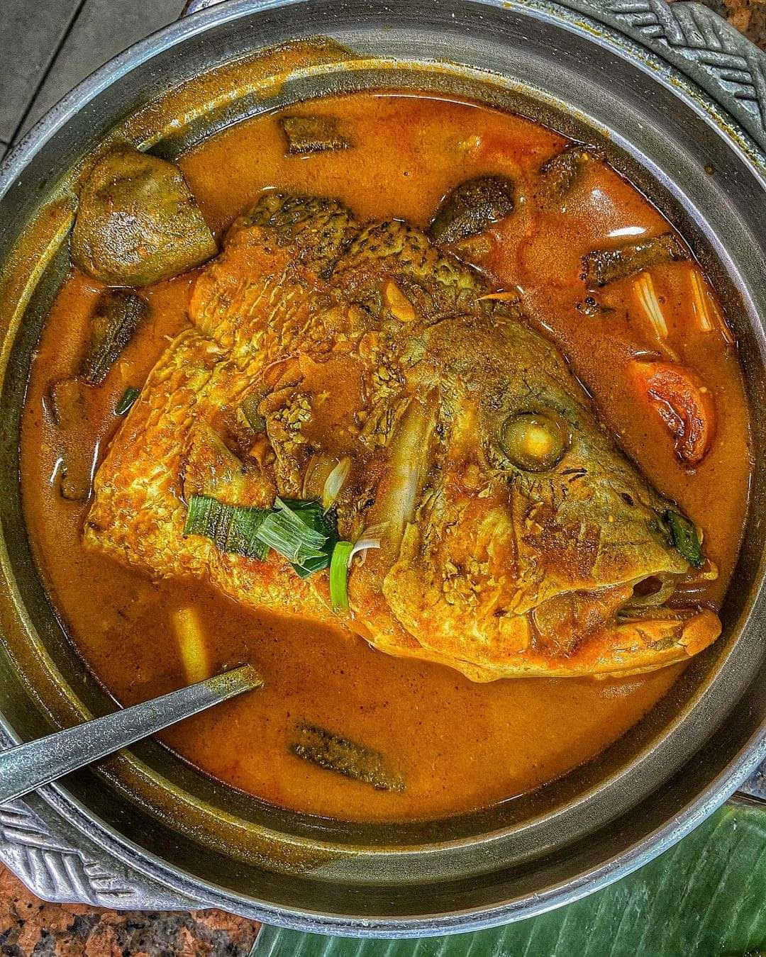 魚頭咖喱頂視圖 壁紙 — 一鍋冒煙的濃郁橙色魚咖喱，內有完整魚頭和香料，盛載於金屬鍋中。