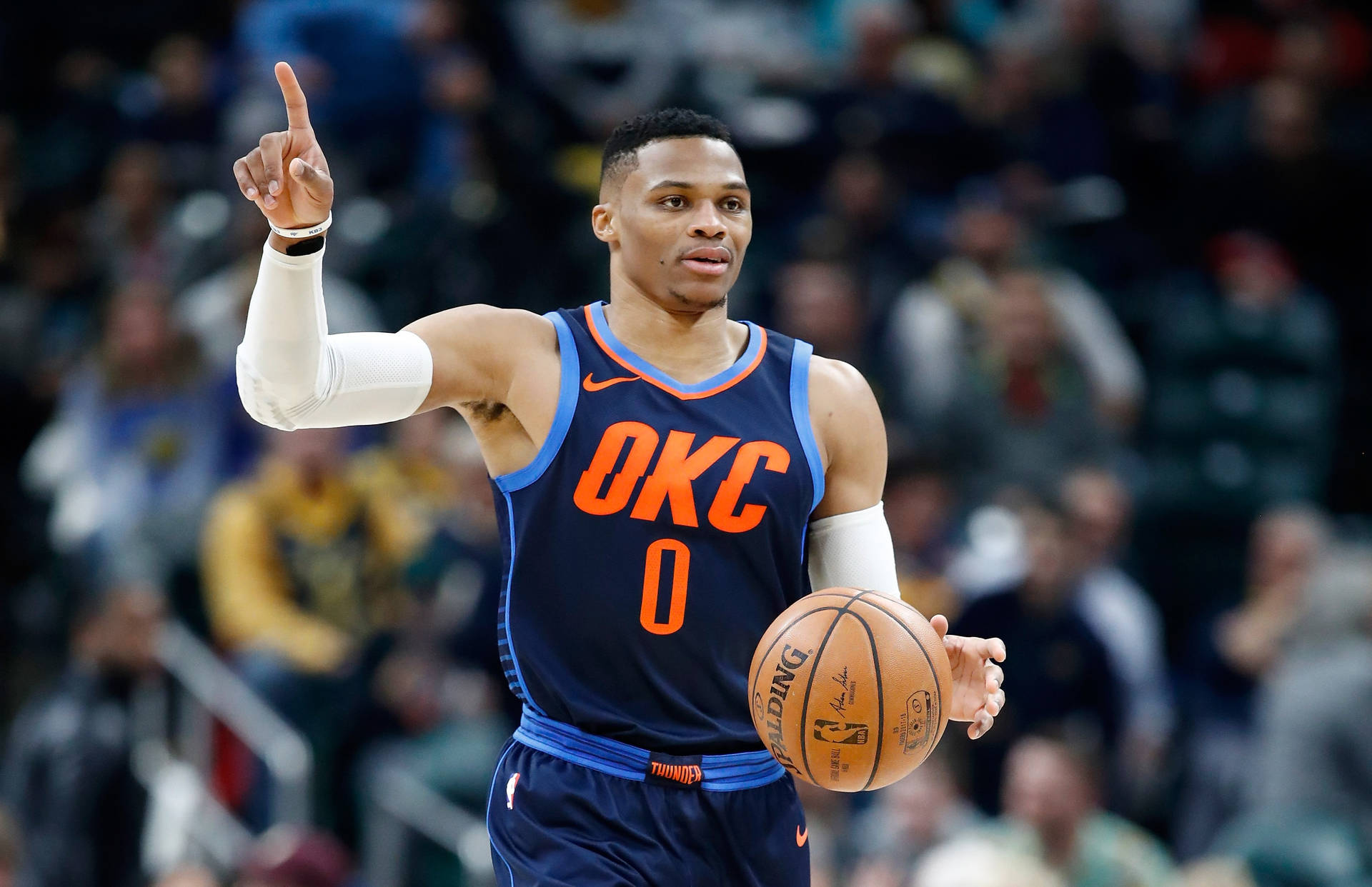 身穿OKC球衣的籃球運動員在比賽中拿著球並向上指。