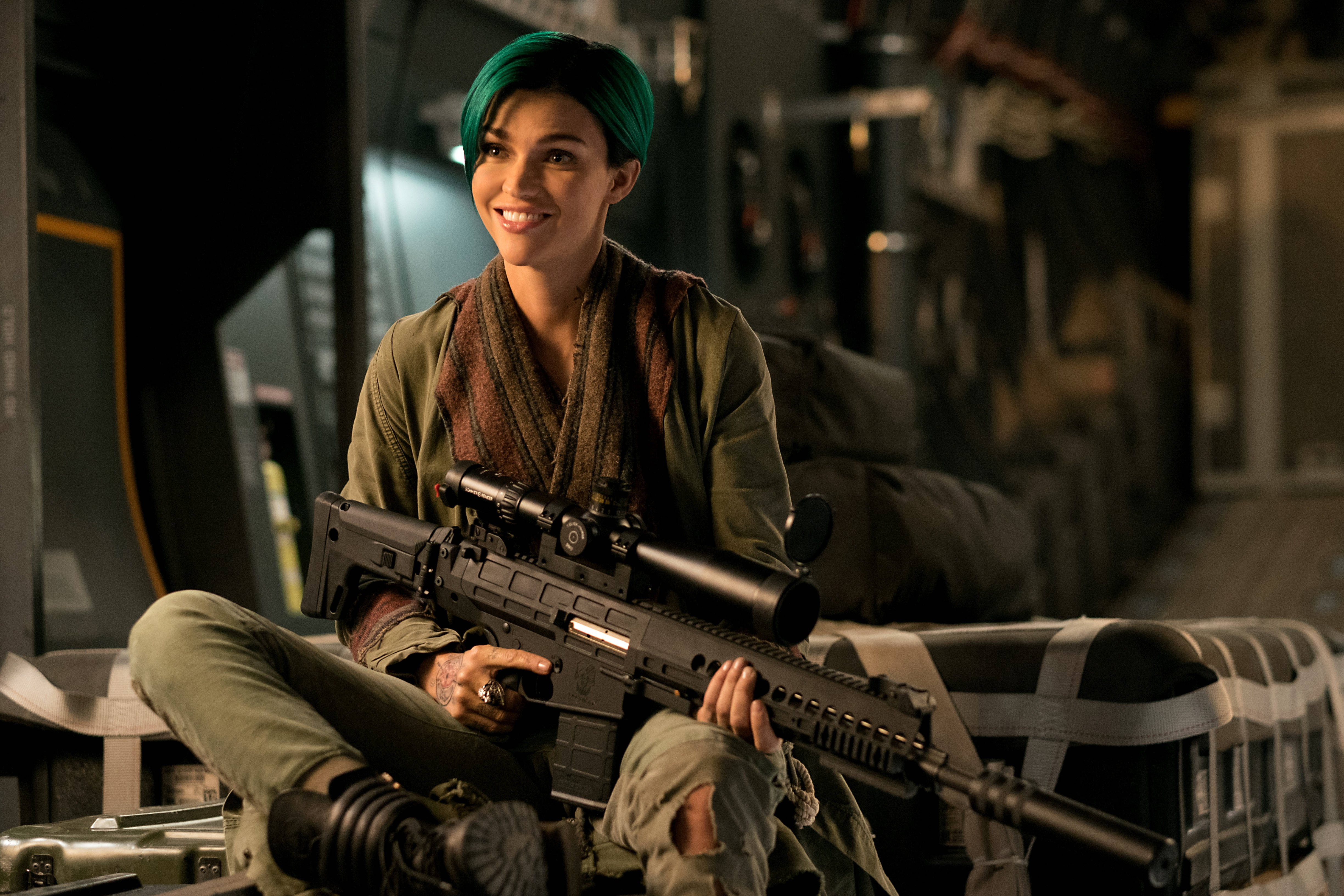 魯比·羅斯出演《xXx：重返Xander Cage》 壁紙 — 一位擁有鮮豔綠髮的女性微笑著，在昏暗的工業環境中手持狙擊步槍。