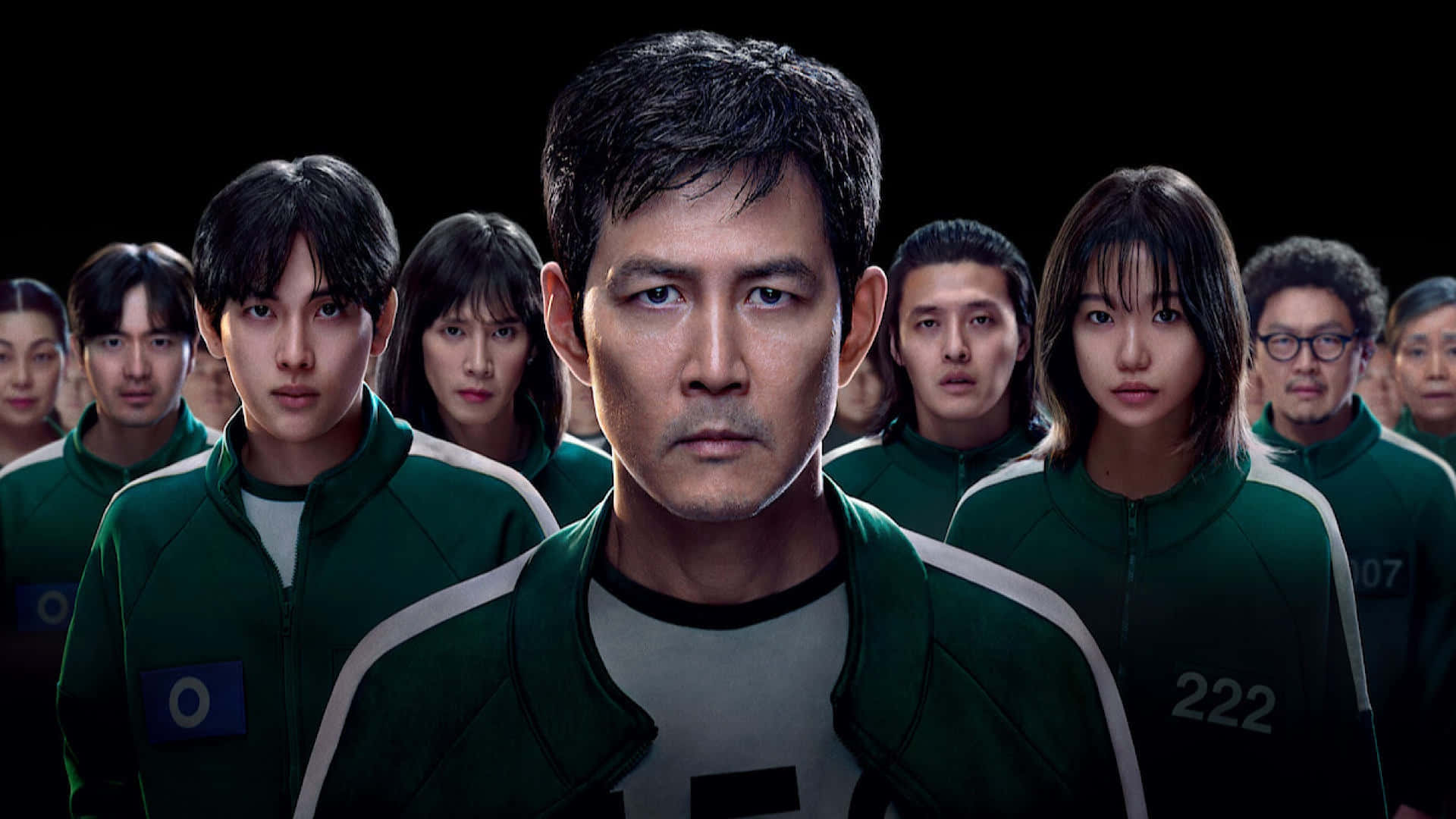 《魷魚遊戲》第二季演員陣容 壁紙 — 一群穿著綠色號碼外套的參賽者，在黑色背景下凝視著。