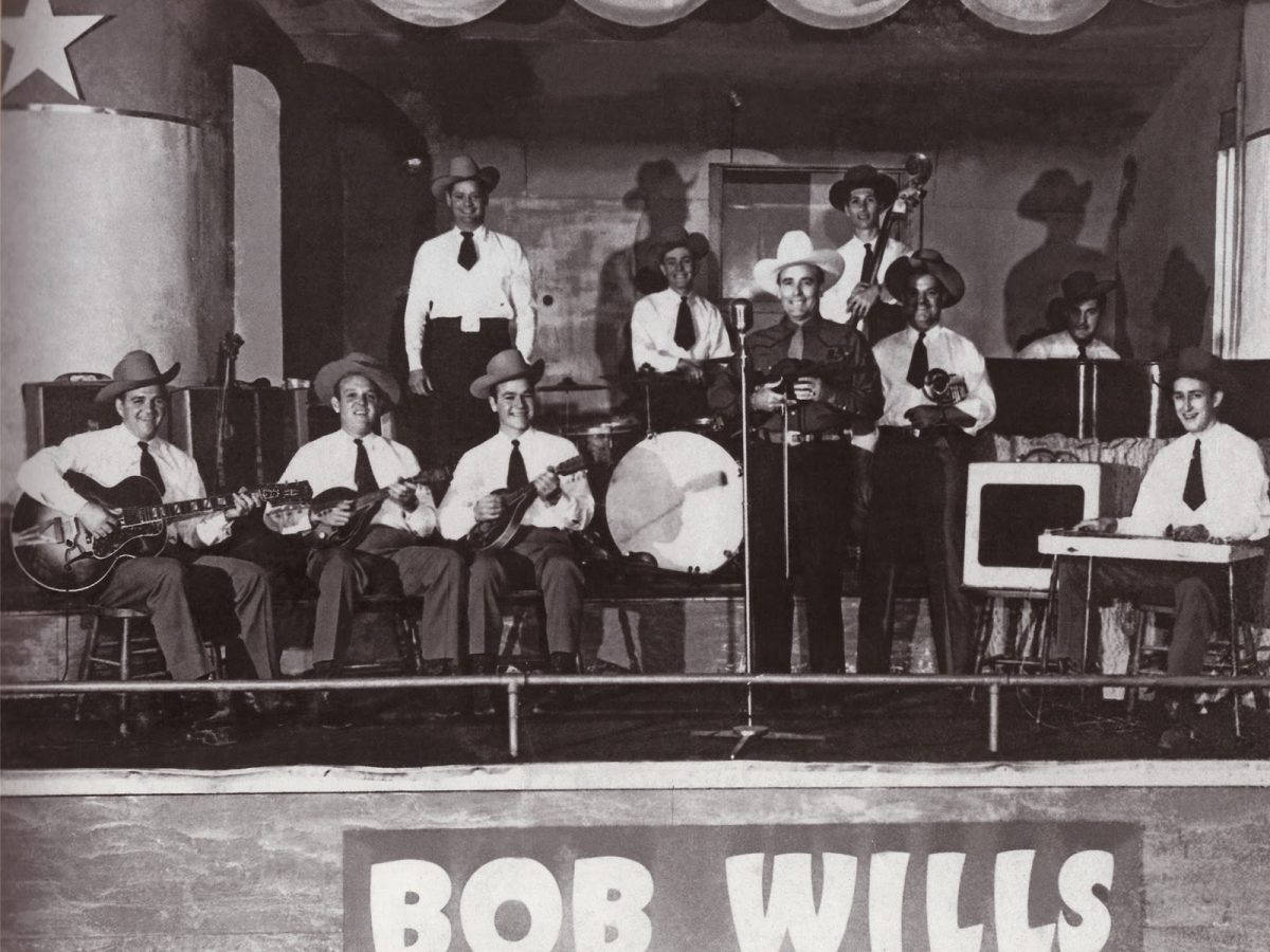鮑勃·威爾斯與德克薩斯玩伴樂隊演奏樂器 壁紙 — 一張Bob Wills及其樂隊在舞台上表演的復古黑白照片，戴著牛仔帽並使用樂器。