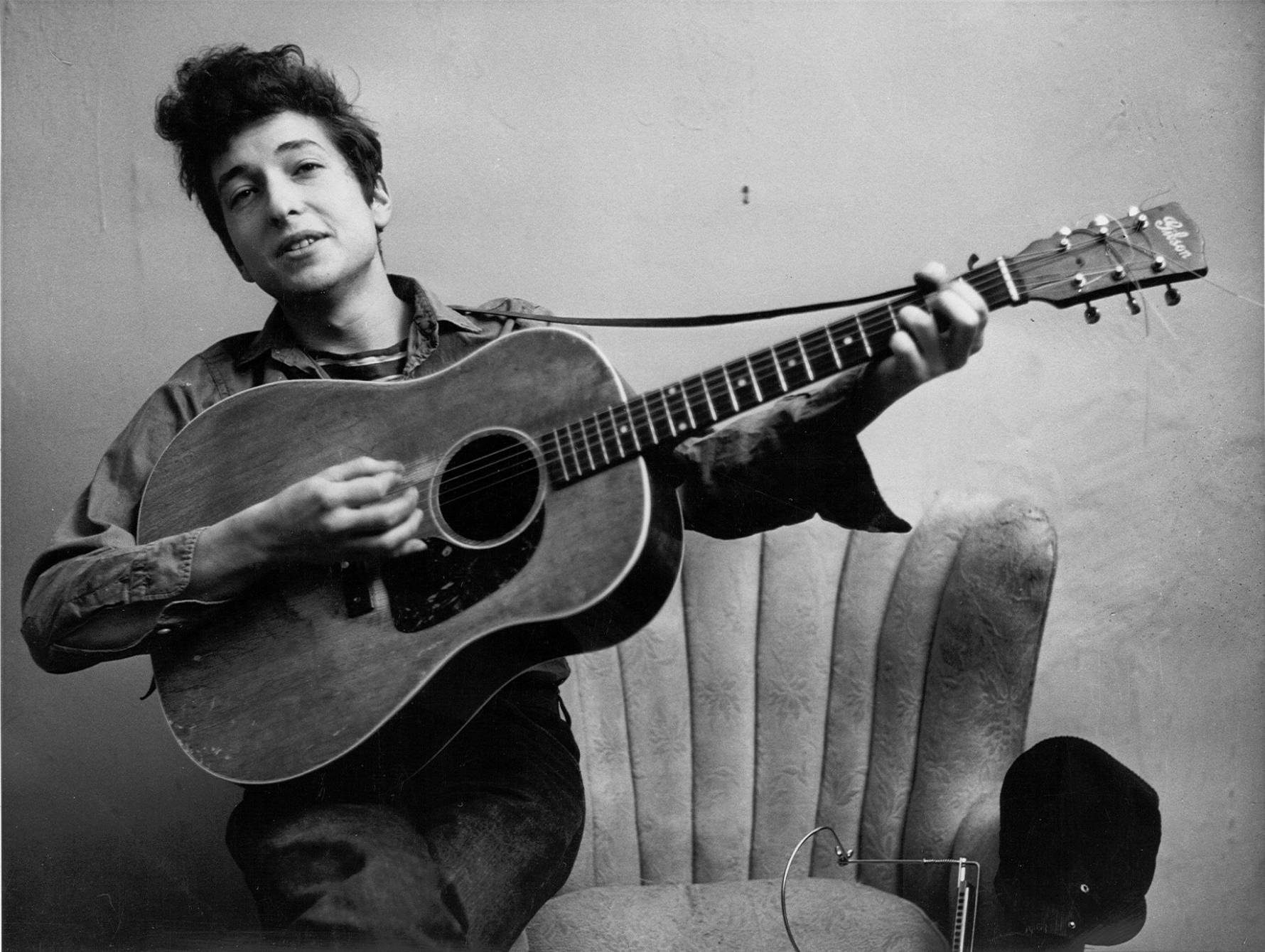 Bob Dylan 在一張黑白工作室肖像照中手持木結他。