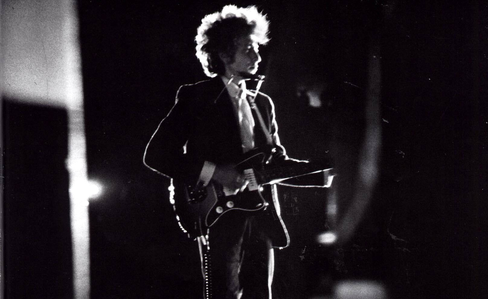Bob Dylan 在黑白照片中於舞台上彈奏電結他。