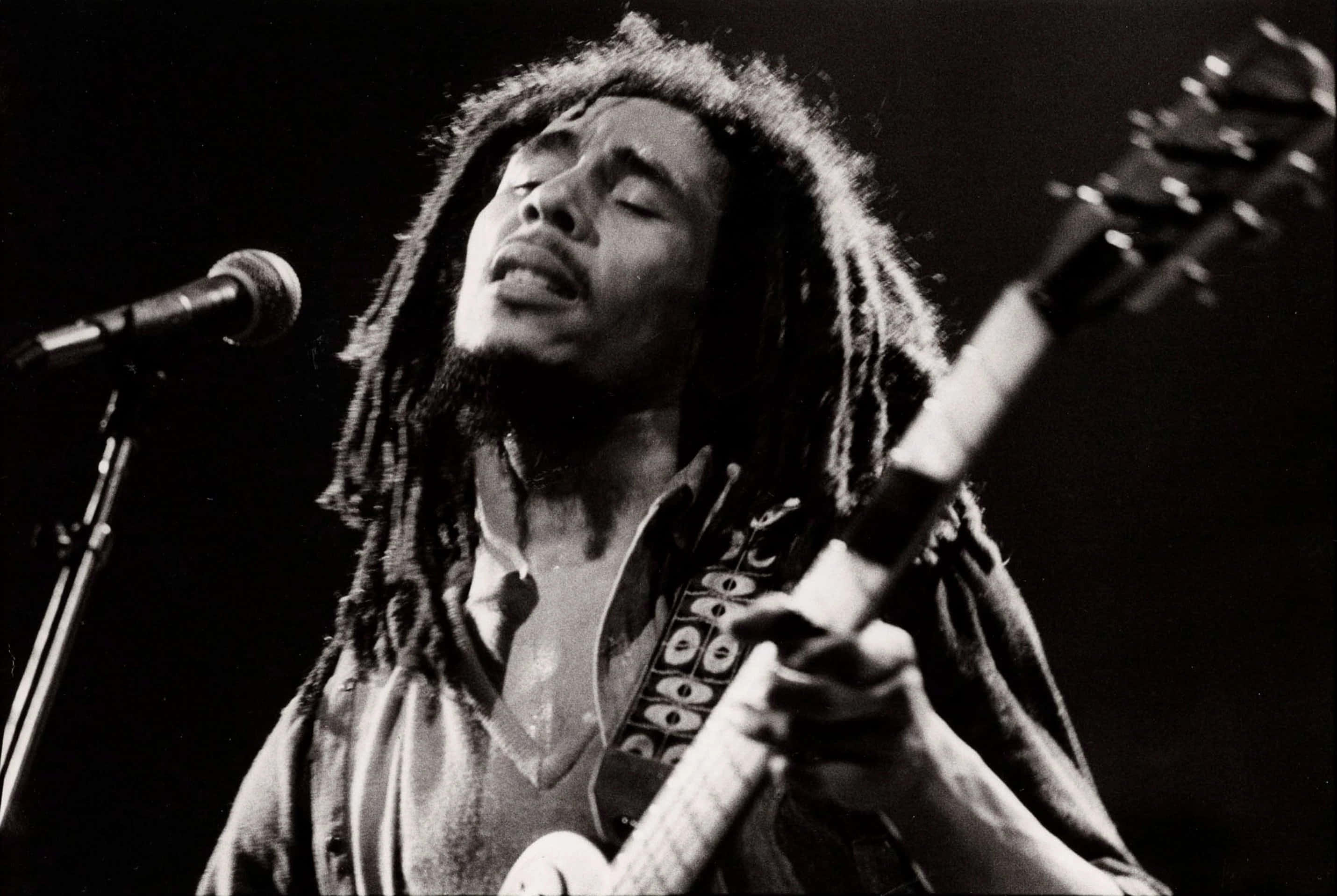 鮑勃·馬利以歌聲抗議 壁紙 — 一張黑白照片捕捉到 Bob Marley 閉著眼睛，一邊彈結他一邊充滿激情地對著咪高峰唱歌。