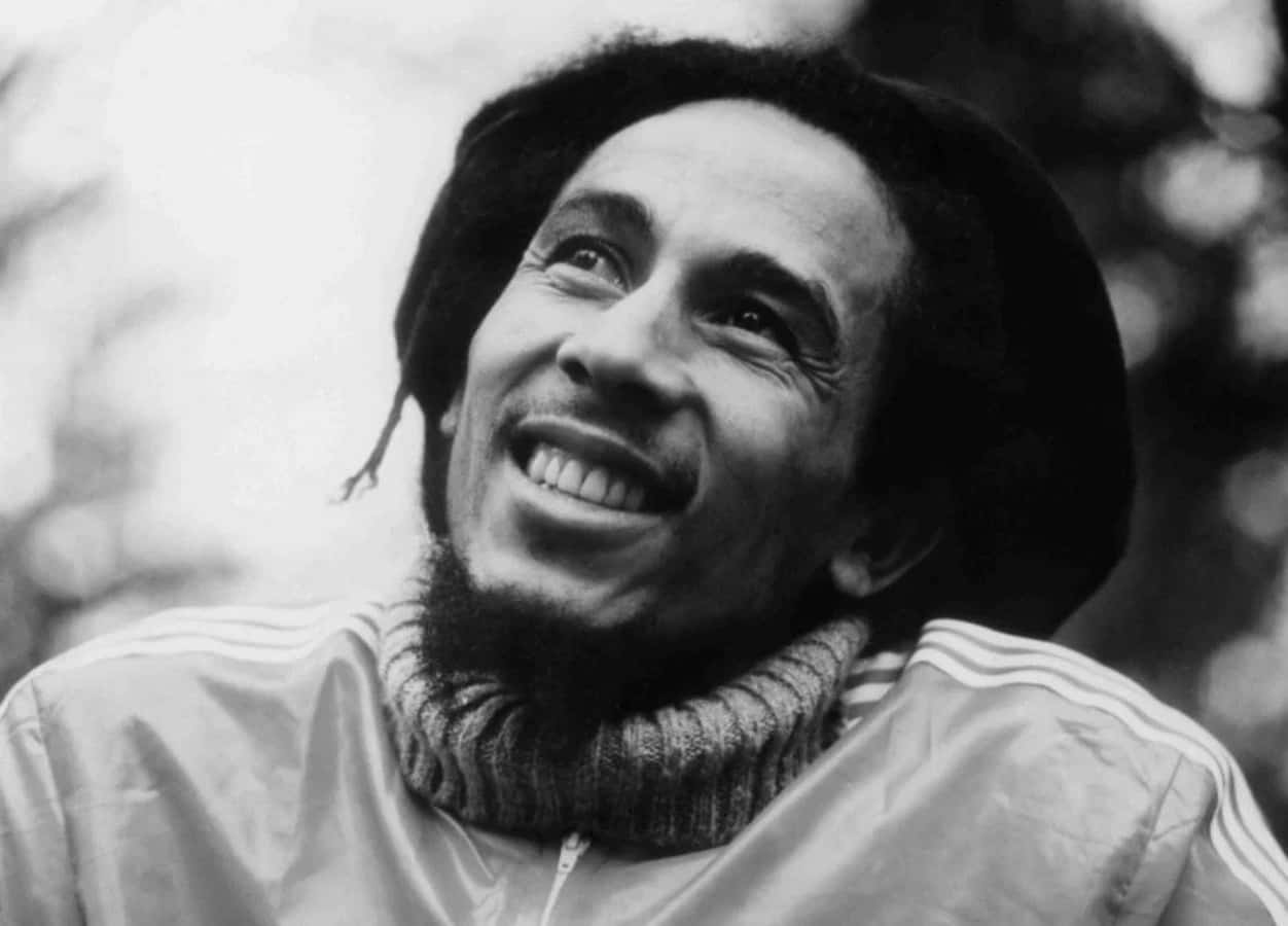 鮑勃·馬利傳遞愛與和平 壁紙 — 一張快樂的黑白肖像，Bob Marley 露出燦爛的笑容，帶有標誌性的辮子和 Adidas 外套。