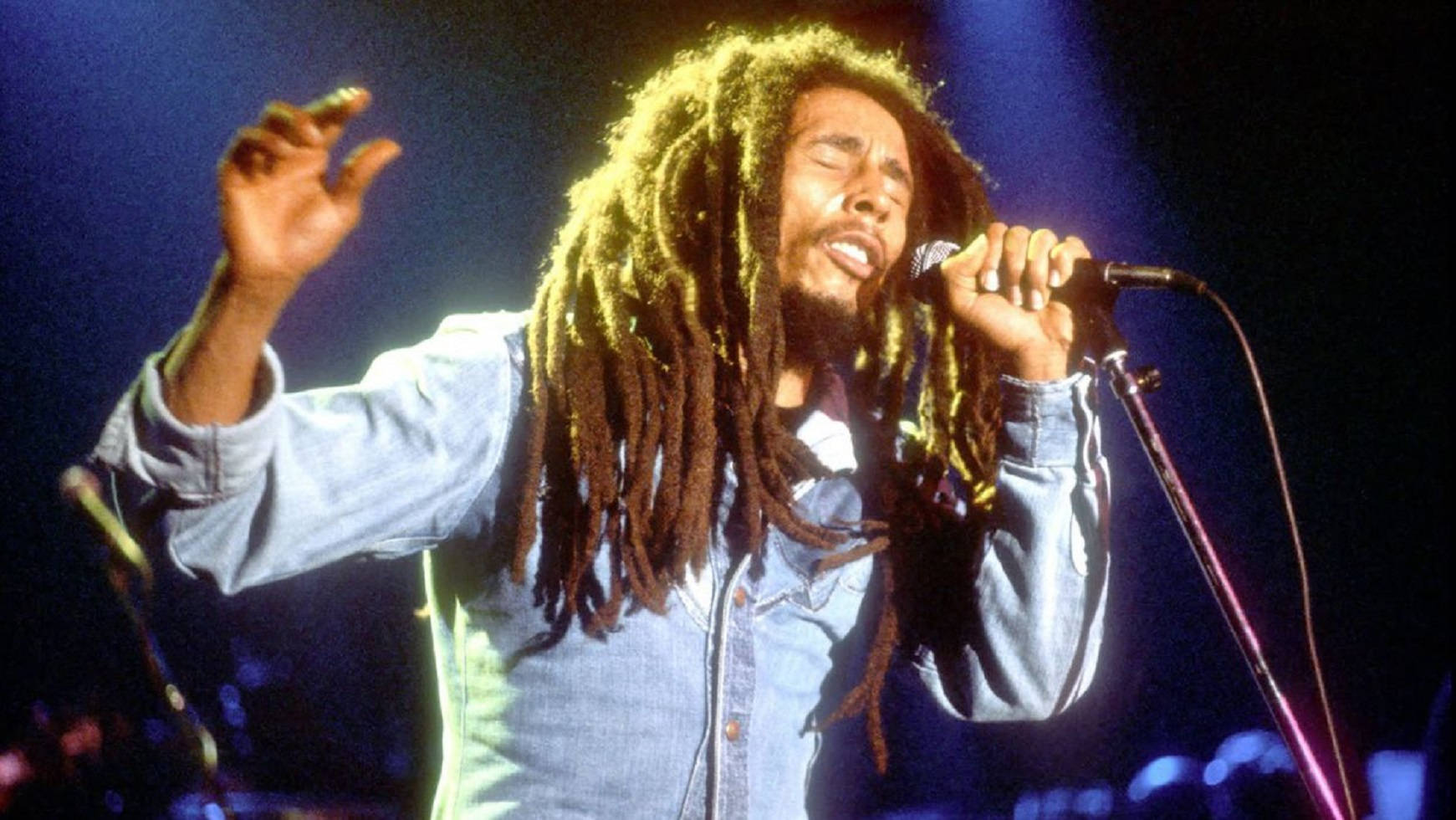 Bob Marley 在舞台上高舉雙臂，閉上眼睛熱情地唱歌。