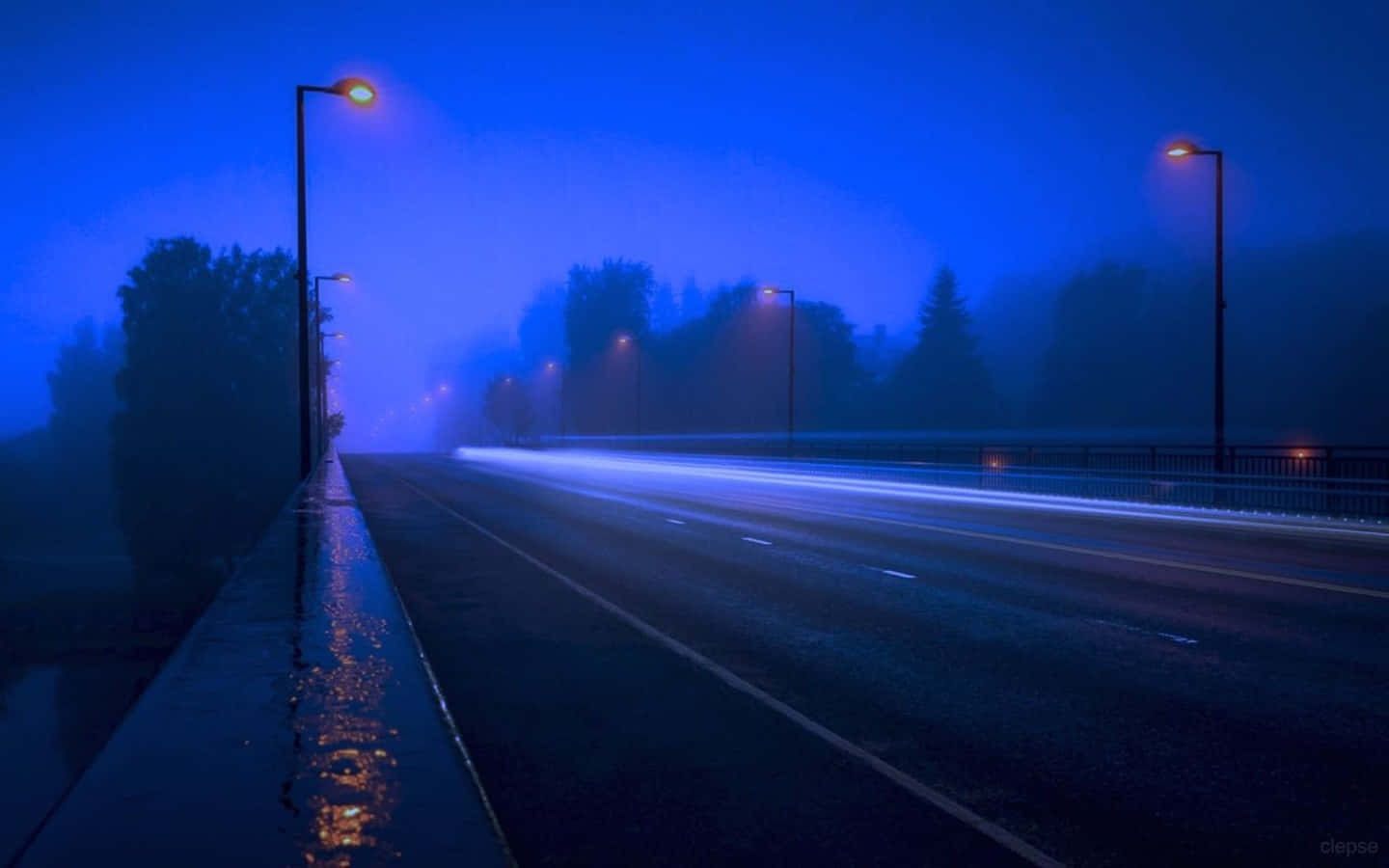 一條霧氣瀰漫的夜晚道路，有發光的街燈和汽車燈光的條紋。