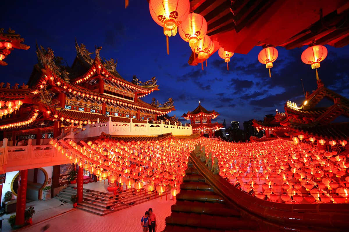 鮮紅燈籠照亮春節慶祝 壁紙 — 一座宏偉的傳統寺廟在黃昏時分被數千盞發光的紅燈籠照亮，燈籠沿著樓梯和屋頂傾瀉而下。
