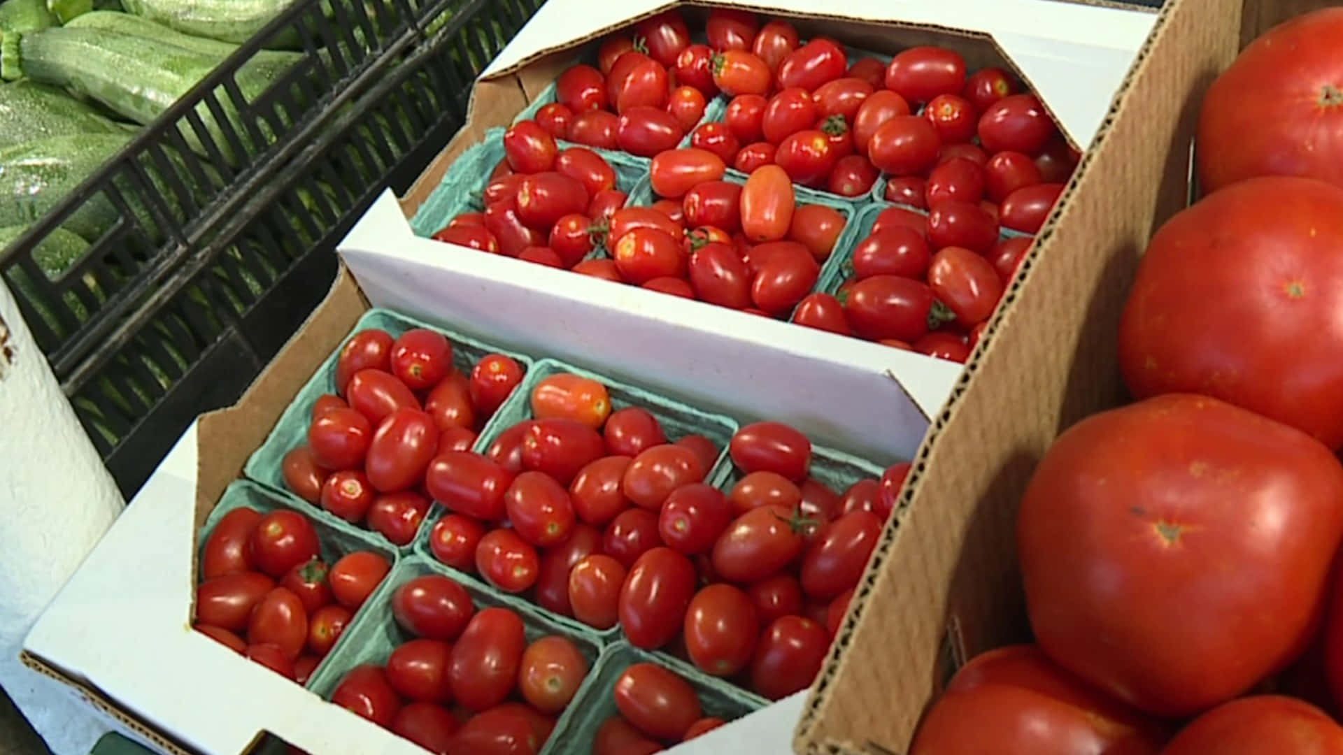 Farmers Market 桌布 壁紙 — 鮮紅色的車厘茄和大型牛茄裝滿市場攤位的紙箱，旁邊有青瓜。