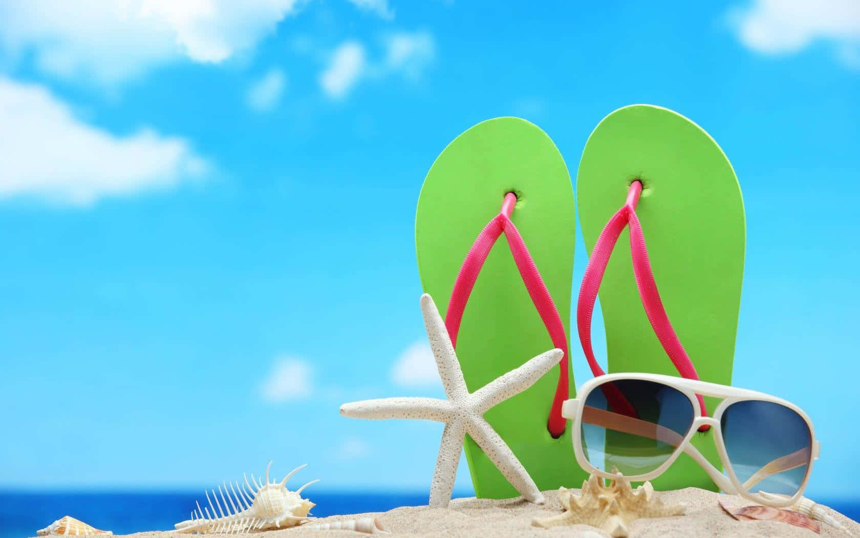 Beach Sandals 桌布 壁紙 — 鮮綠色人字拖配粉紅色帶子和白色太陽眼鏡，放在沙灘上，旁邊有海星和貝殼，天空清澈湛藍。