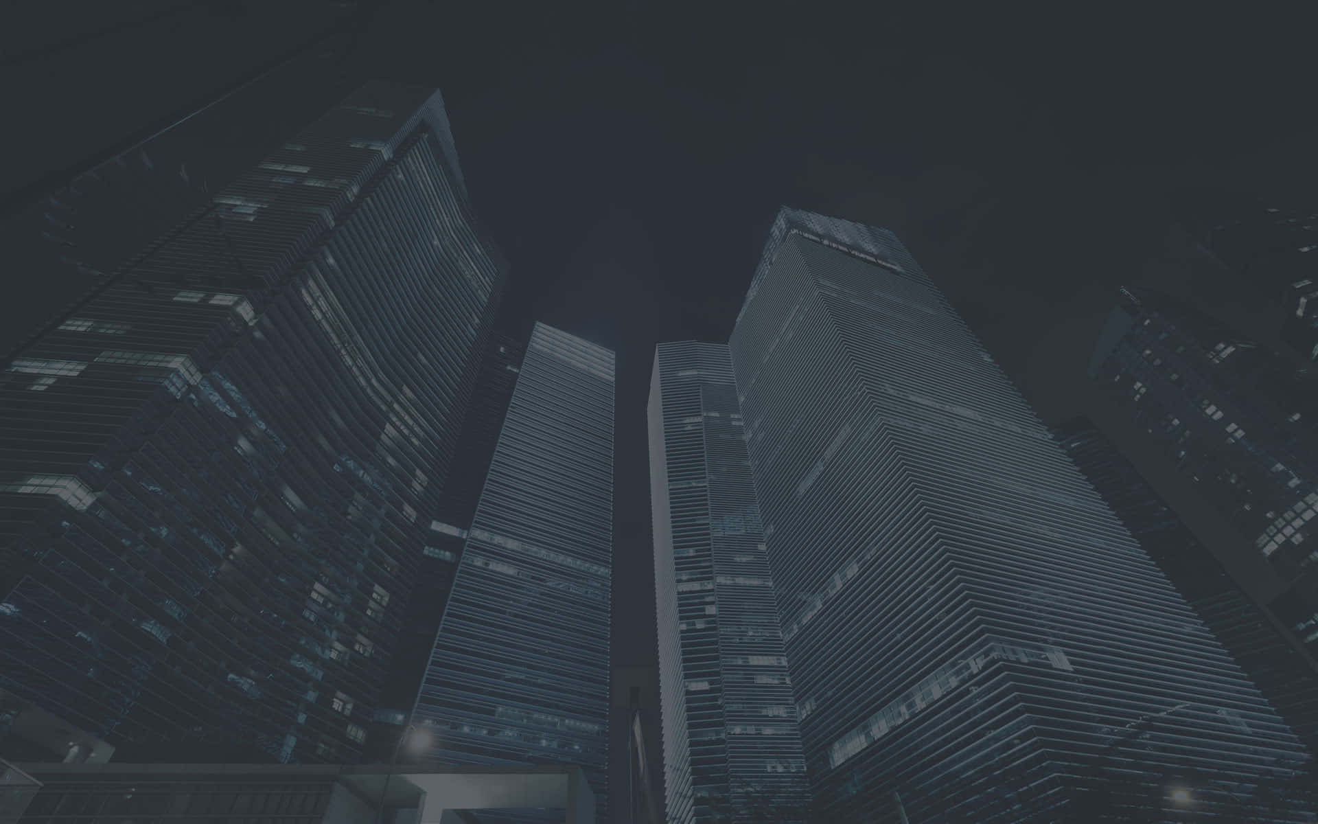 漆黑的都市天際線，高聳的玻璃摩天大樓在夜晚被發光的窗戶照亮。