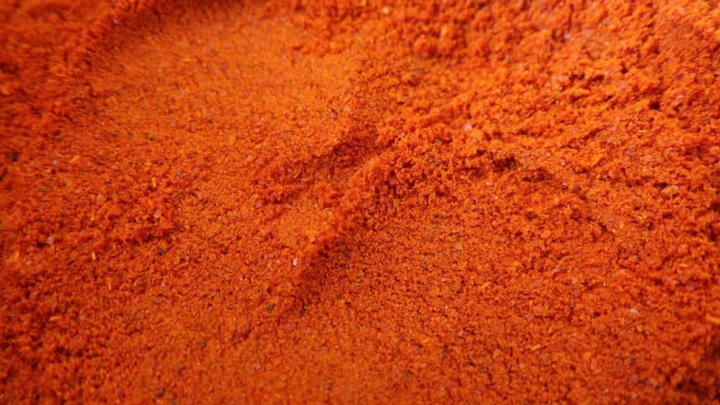 Red Chili Powder 桌布 壁紙 — 鮮豔橙紅色辣椒粉的特寫，帶有紋理顆粒和細微陰影。