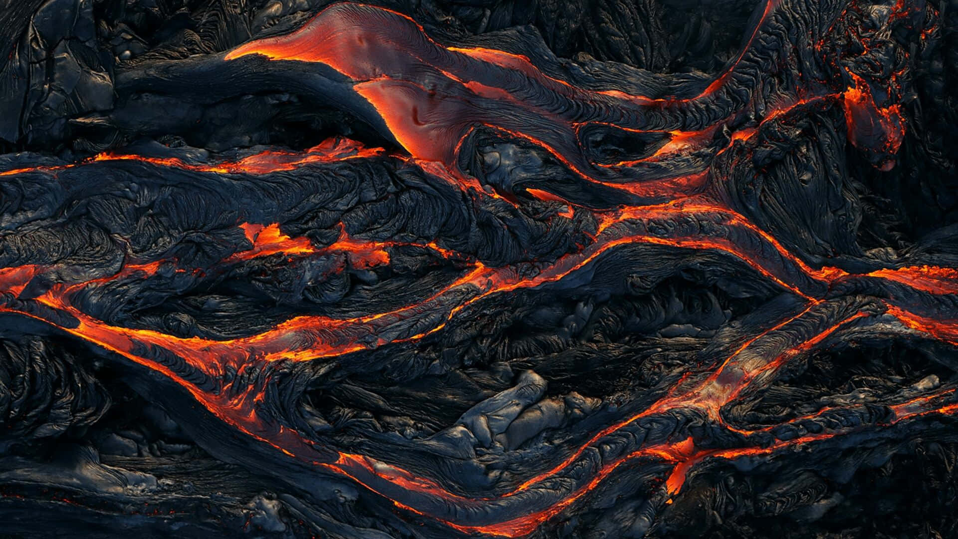 lava 桌布 壁紙 — 鮮豔發光的熔岩河流在崎嶇的黑色火山地形中切割出一幅戲劇性的自然景象。
