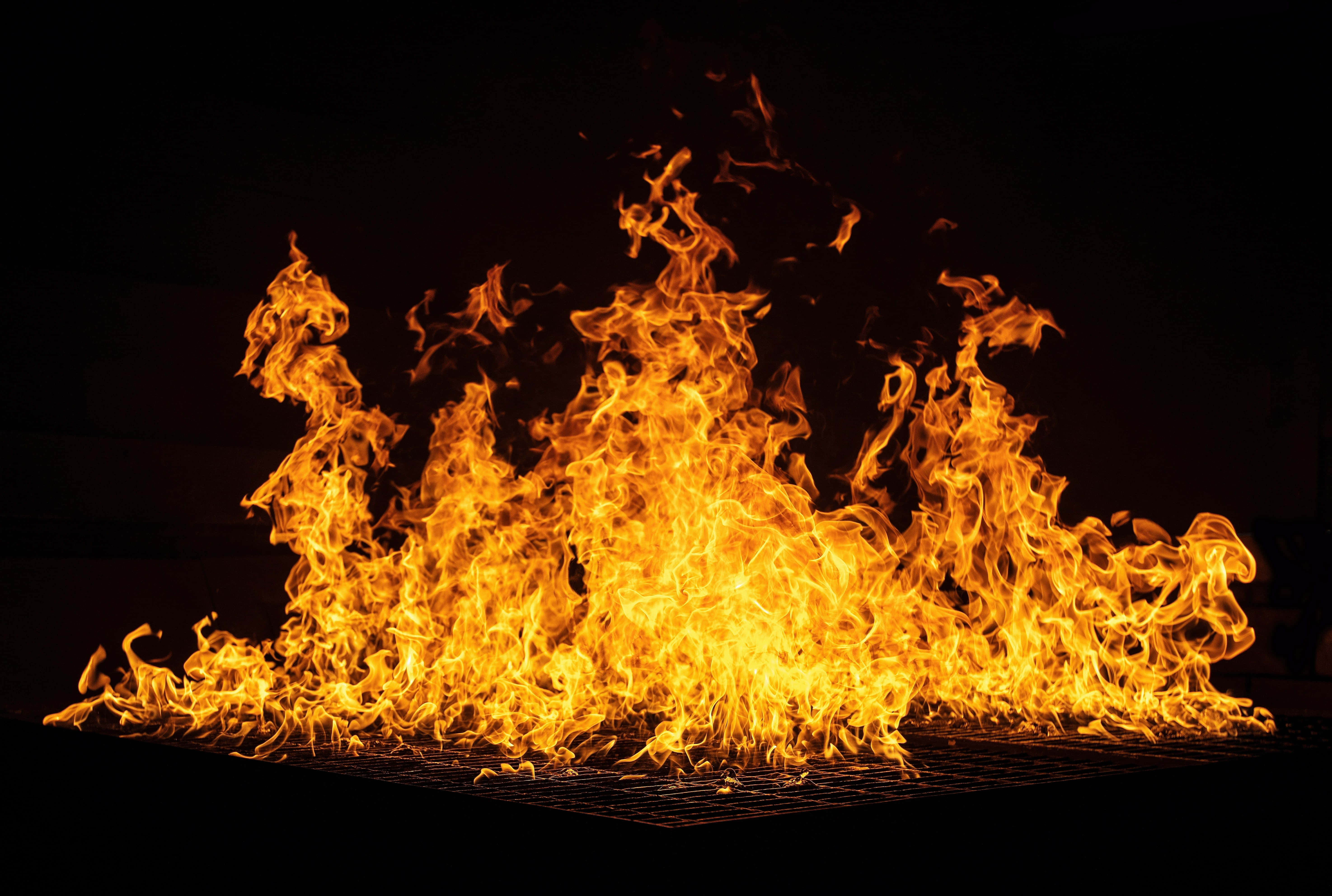 Fall Bonfire 桌布 壁紙 — 鮮豔的橙色和黃色火焰在漆黑的背景下向上翻湧，營造出戲劇性且強烈的視覺效果。