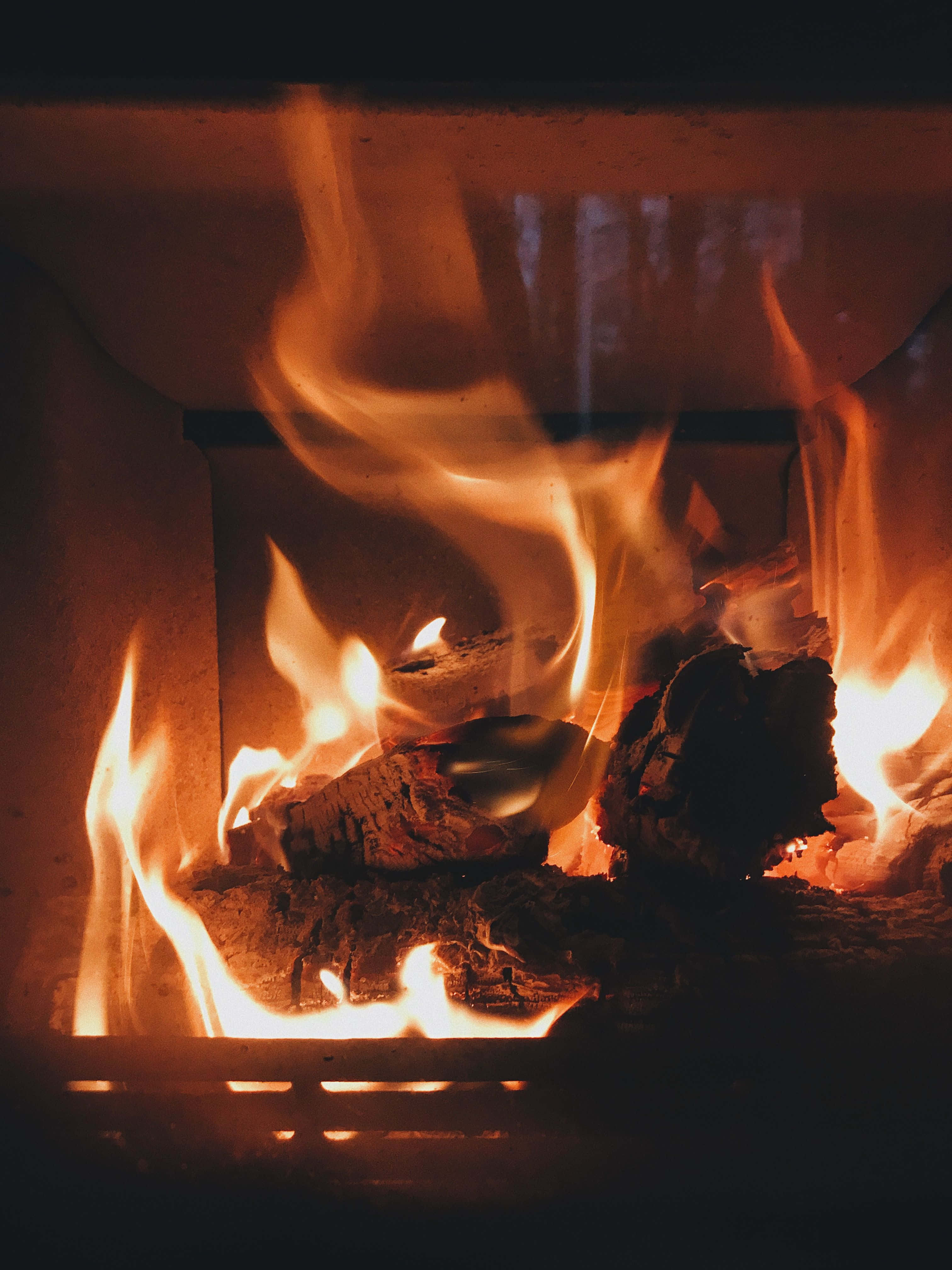 Cozy Fire 桌布 壁紙 — 鮮豔的橙色火焰在壁爐內熾熱的餘燼上舞動，為周圍的木柴投下溫暖的光芒。