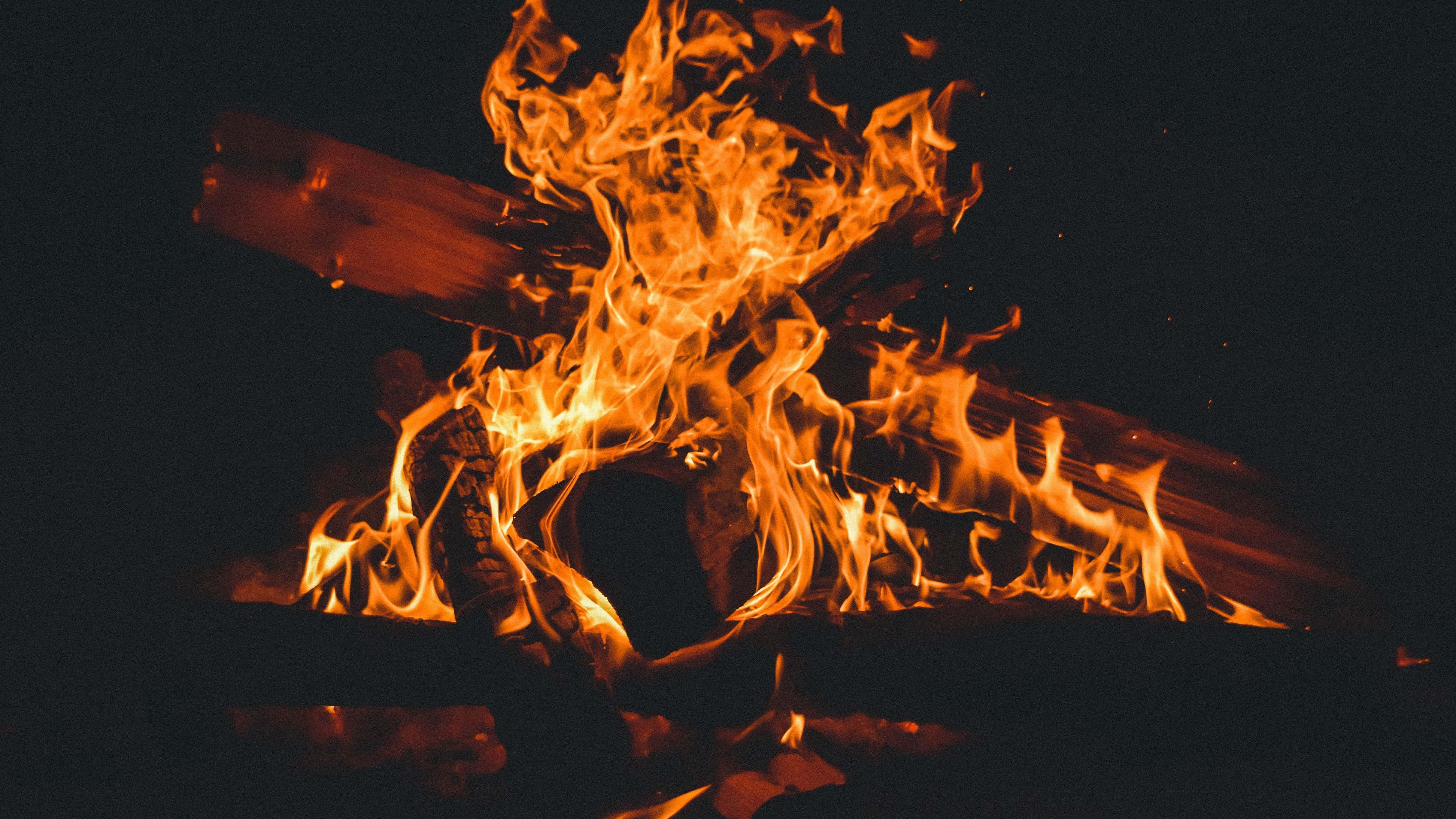 燃燒 桌布 壁紙 — 鮮豔的橙色火焰在漆黑的夜空背景下，圍繞著燃燒的木柴跳躍舞動。