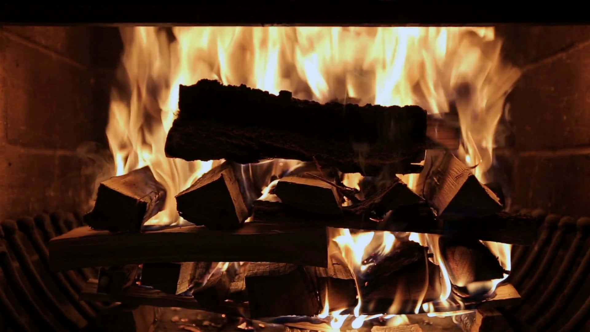 Cozy Fire 桌布 壁紙 — 鮮豔的橙色火焰在石壁爐中的深色木頭周圍跳躍，將溫暖的光線投射在磚牆上。