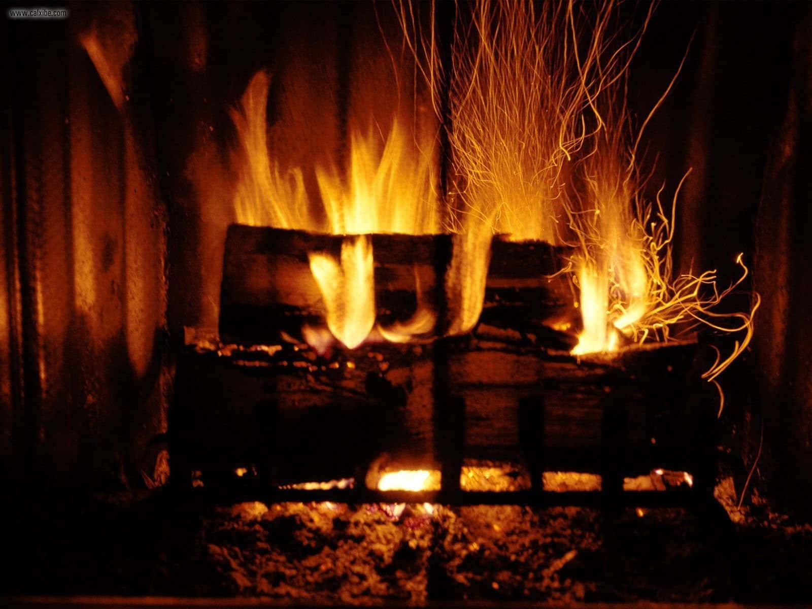 Cozy Fire 桌布 壁紙 — 鮮豔的橙色火焰在黑暗壁爐內燃燒的木頭上跳躍並發出劈啪聲，將溫暖的光芒投射到周圍的木頭上。