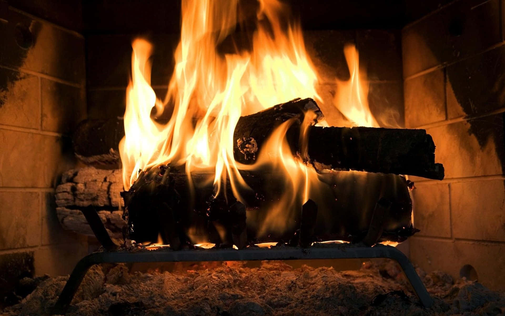 Cozy Fire 桌布 壁紙 — 鮮豔的橙色火焰從石壁爐內燃燒的木柴中躍出，將溫暖的光芒投射在周圍的磚塊上。