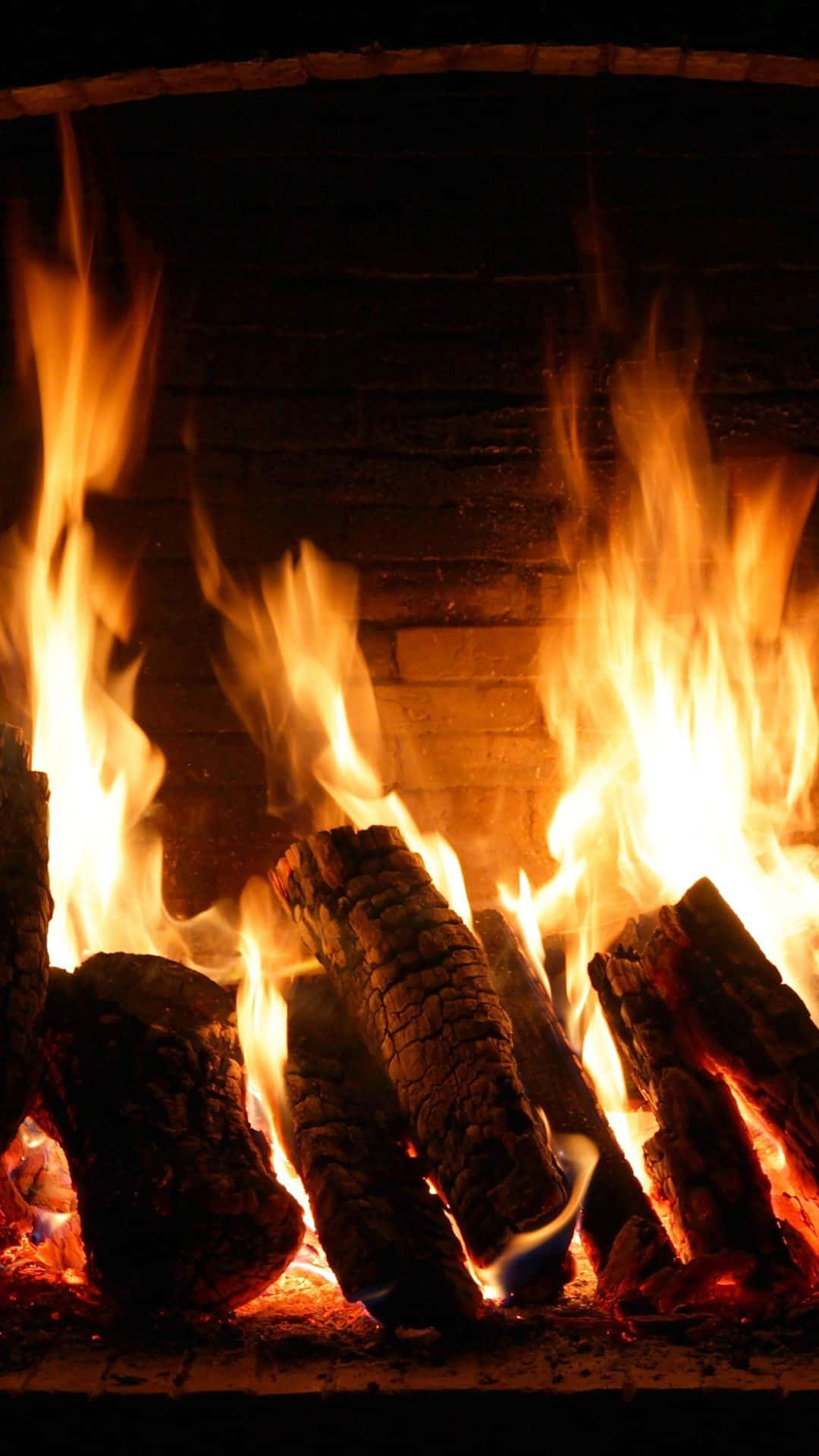 Cozy Fire 桌布 壁紙 — 鮮豔的橙色火焰從黑暗磚砌壁爐內噼啪作響的木柴中躍起，散發出溫暖的光芒。